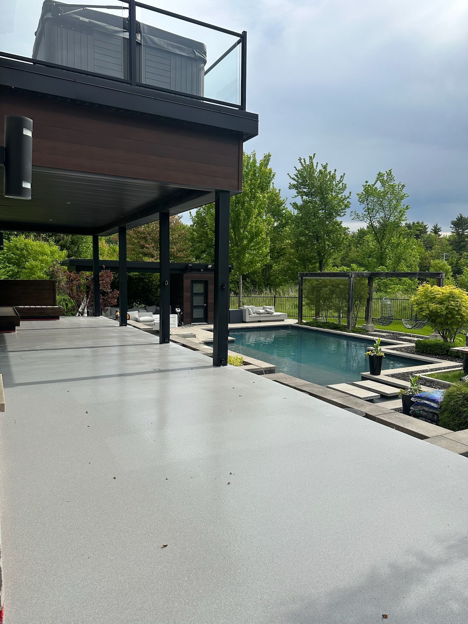 Patio spacieux avec piscine, arbres et architecture moderne par temps couvert.