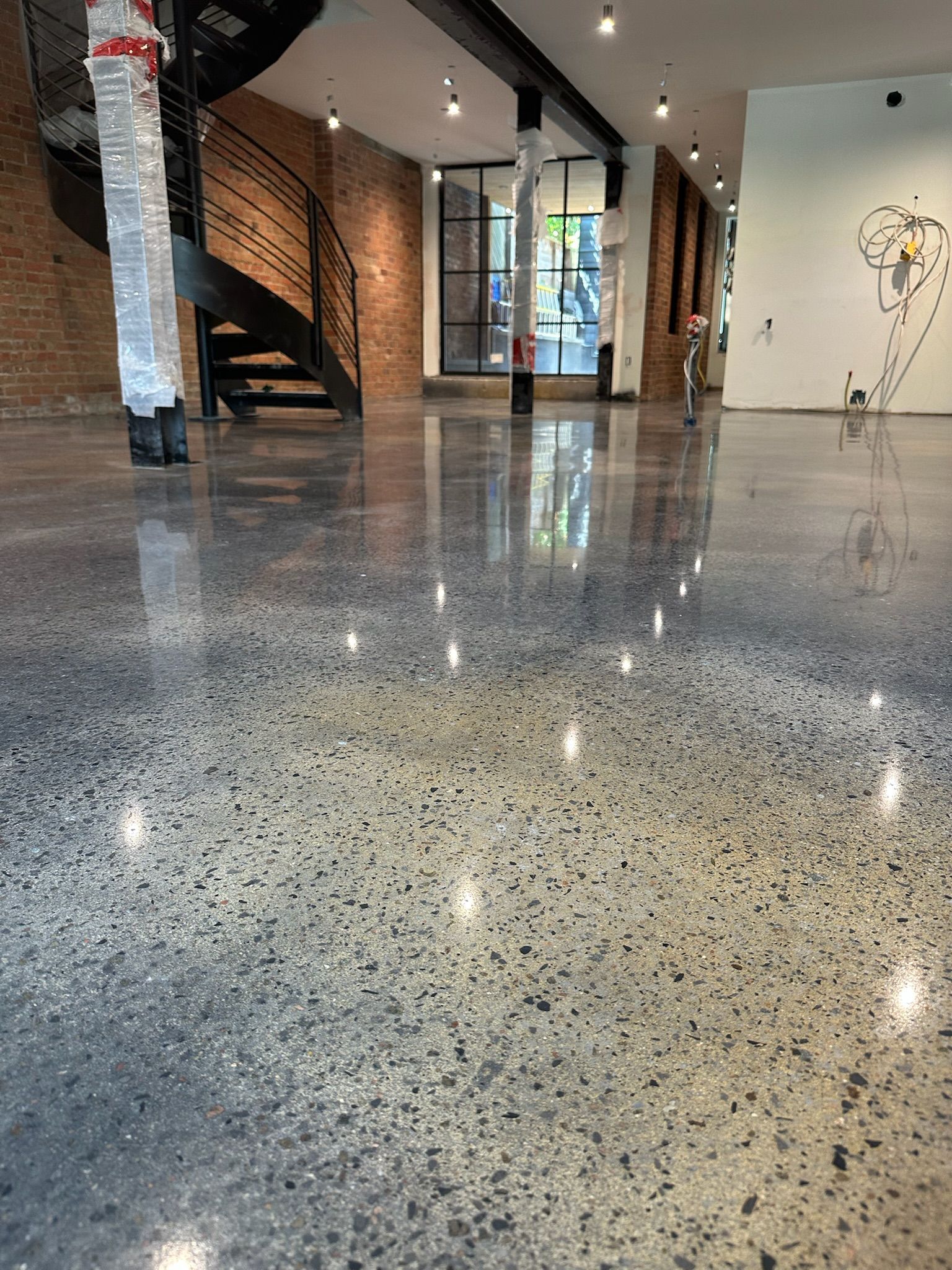 Sol en béton poli dans un intérieur ouvert, avec un escalier et un mur de briques visibles.