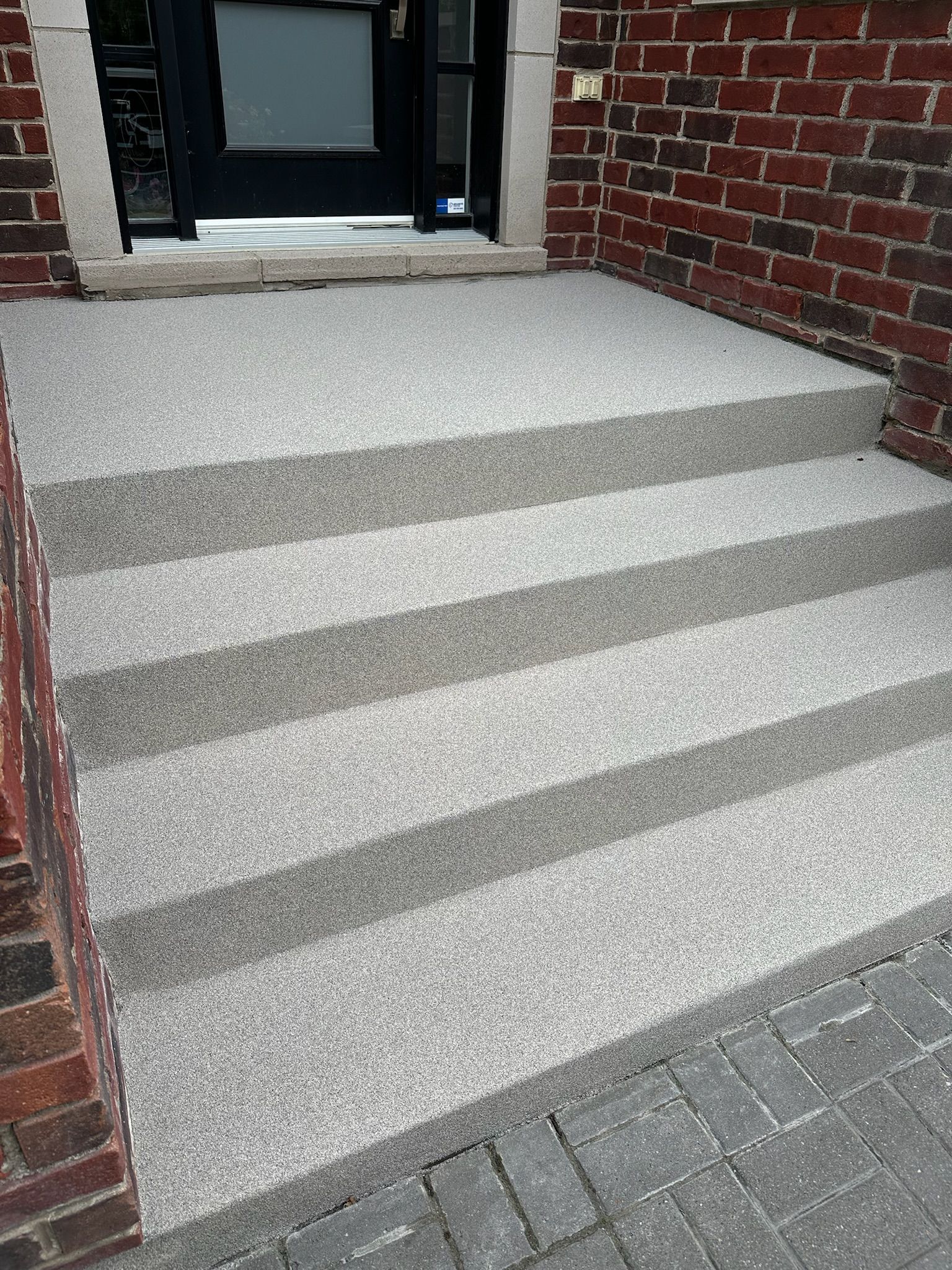 Escalier extérieur au revêtement gris moucheté menant à une porte, entouré de murs de briques.