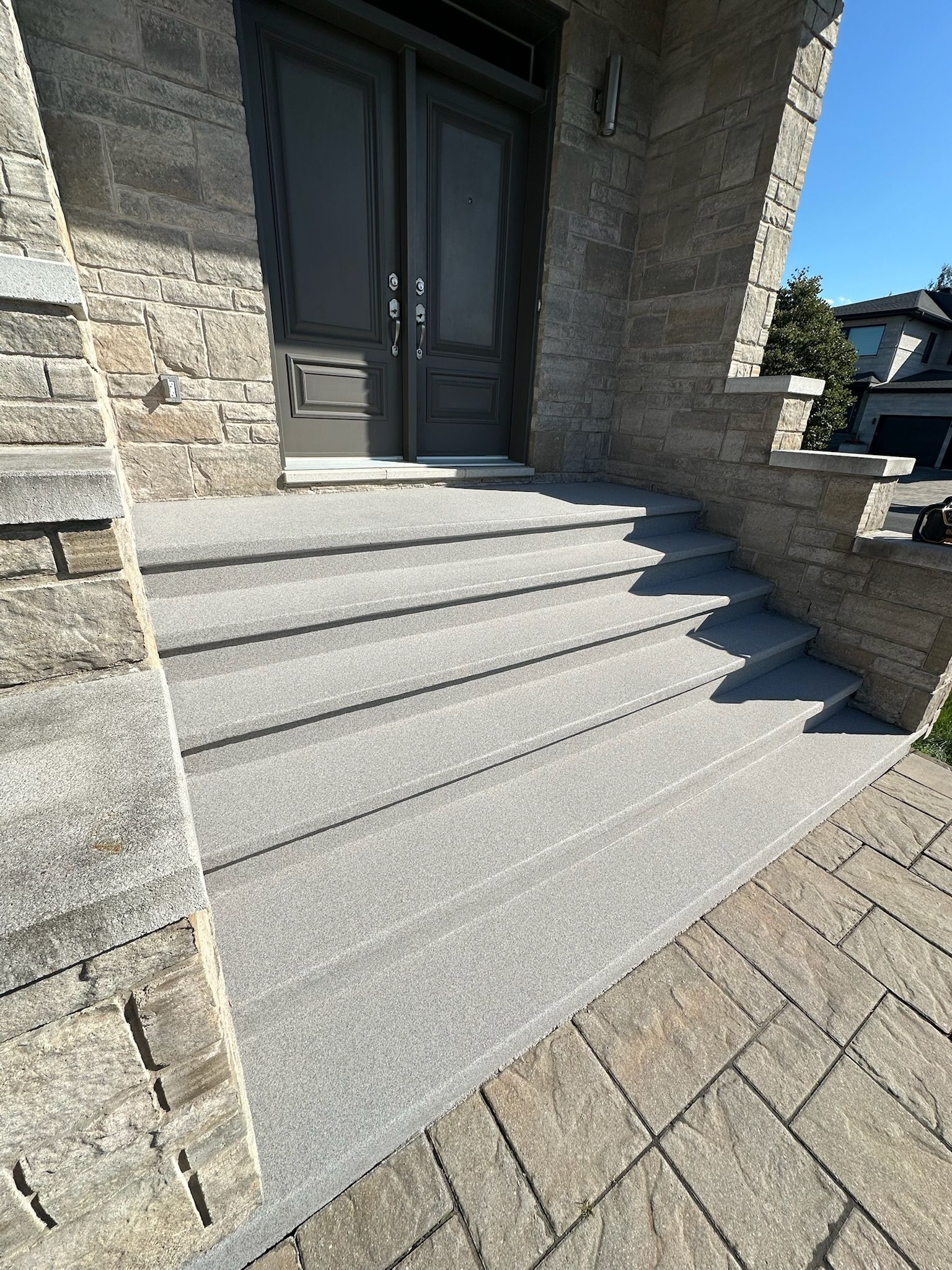 Entrée en façade de pierre avec marches grises menant à des portes doubles.