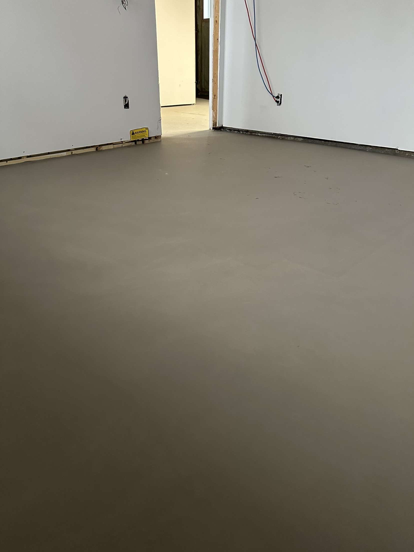 Pièce vide au sol gris lisse et aux murs blancs, vue à travers une porte ouverte.