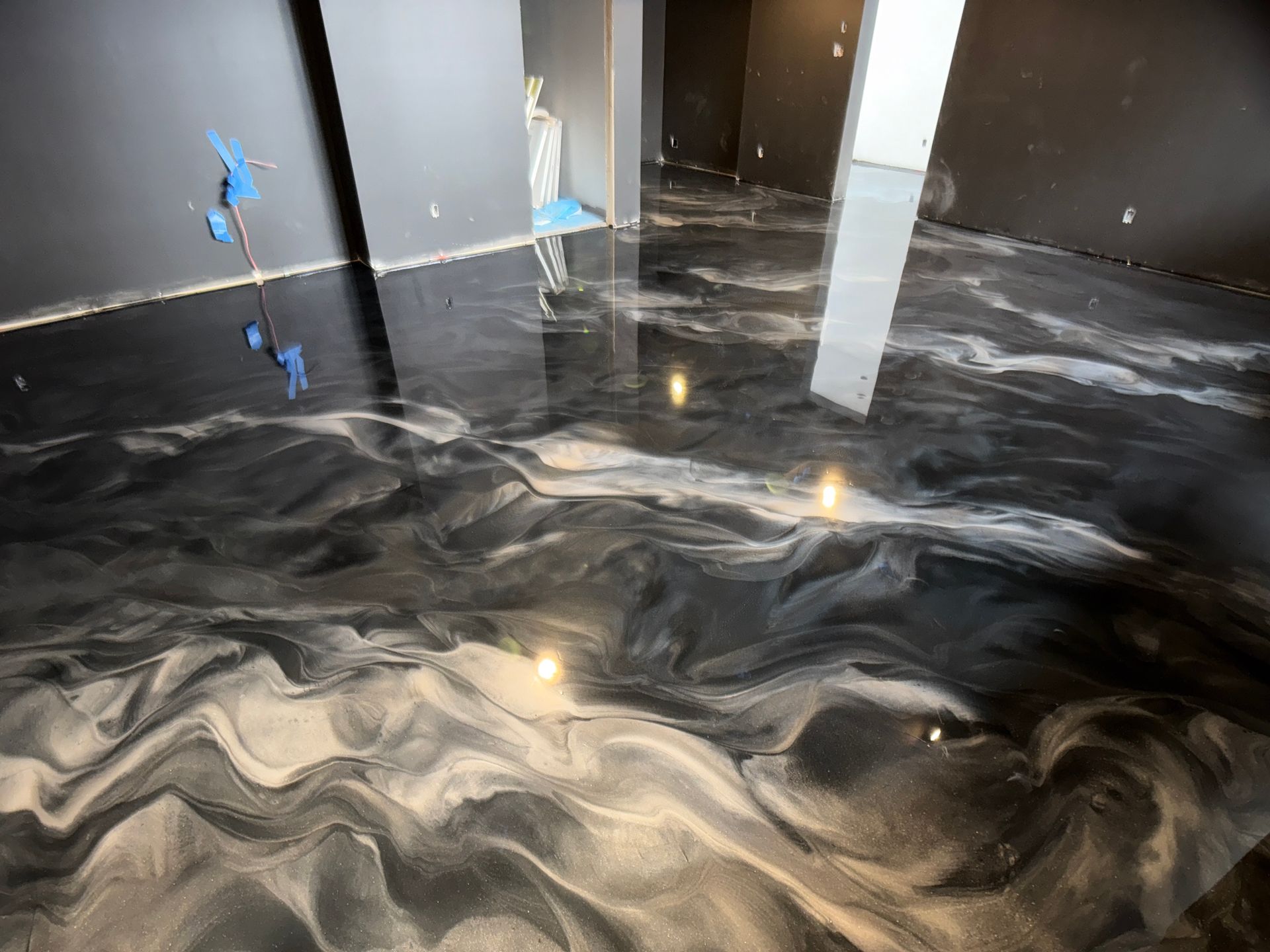 Sol époxy métallique avec motifs tourbillonnants noirs et argentés dans une pièce inachevée.
