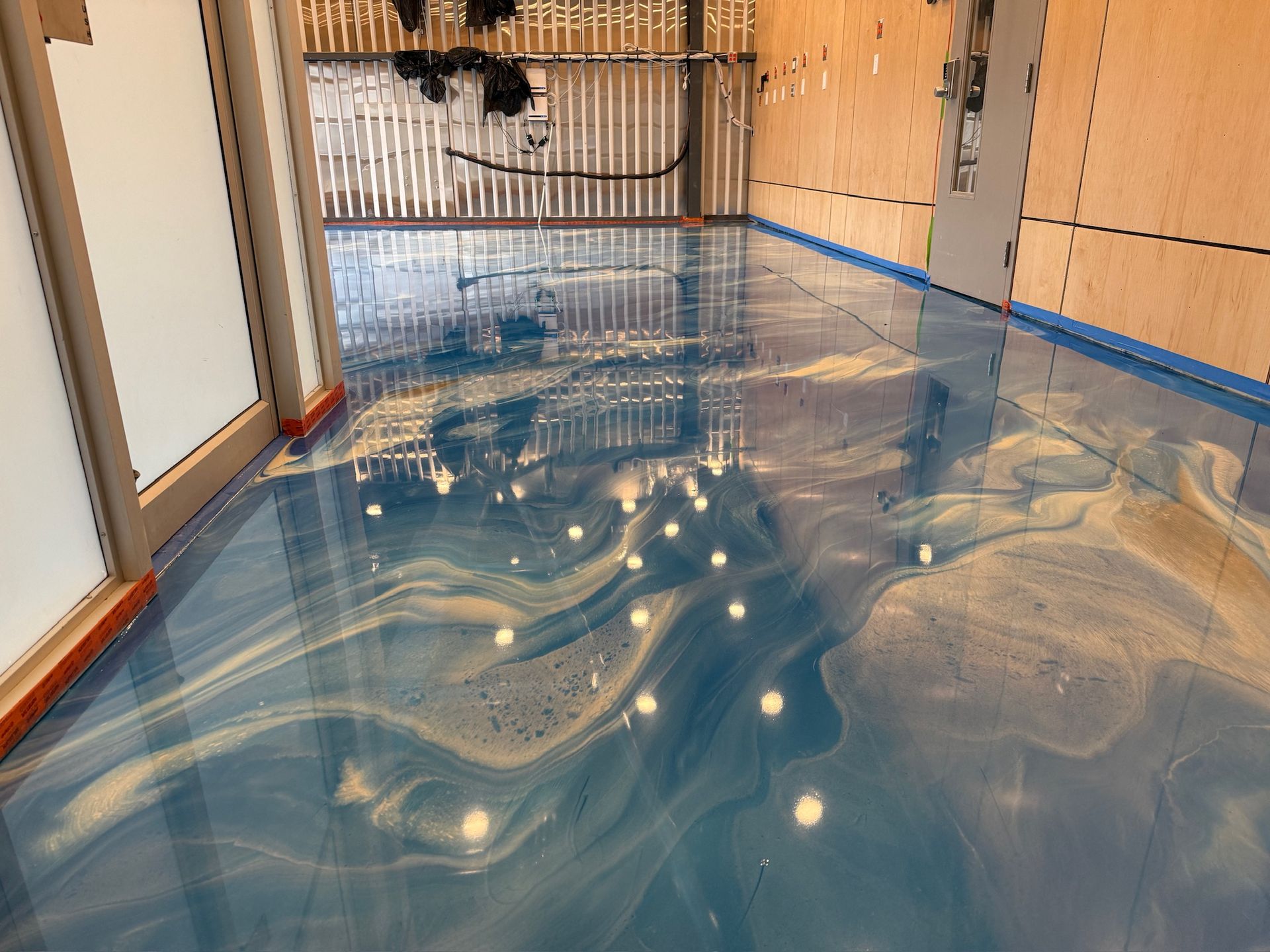 Sol époxy bleu et or avec motifs tourbillonnants, dans une pièce aux murs en panneaux de bois.