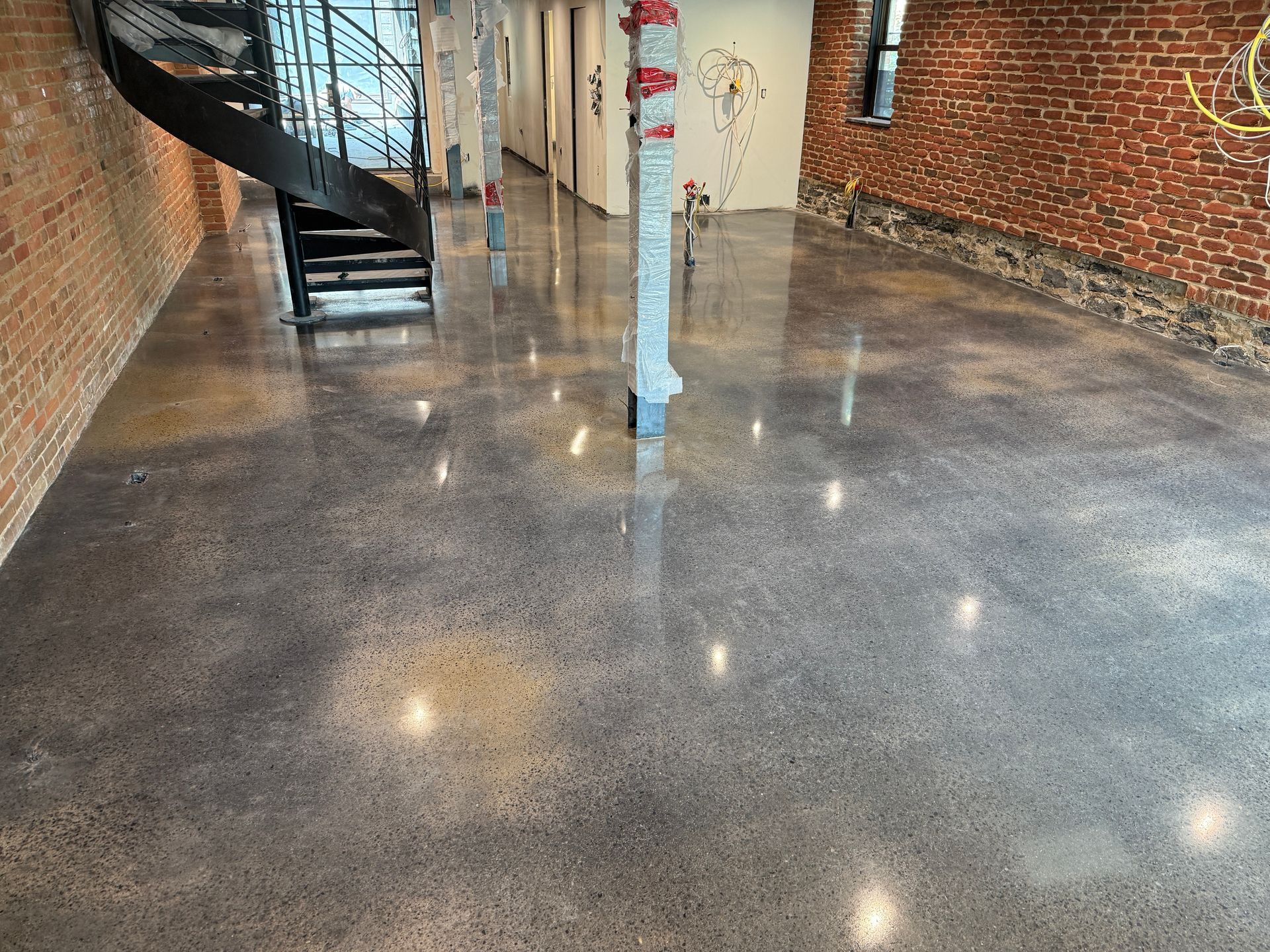 Sol en béton ciré dans un grand espace industriel, murs en briques apparentes, escalier en colimaçon noir.