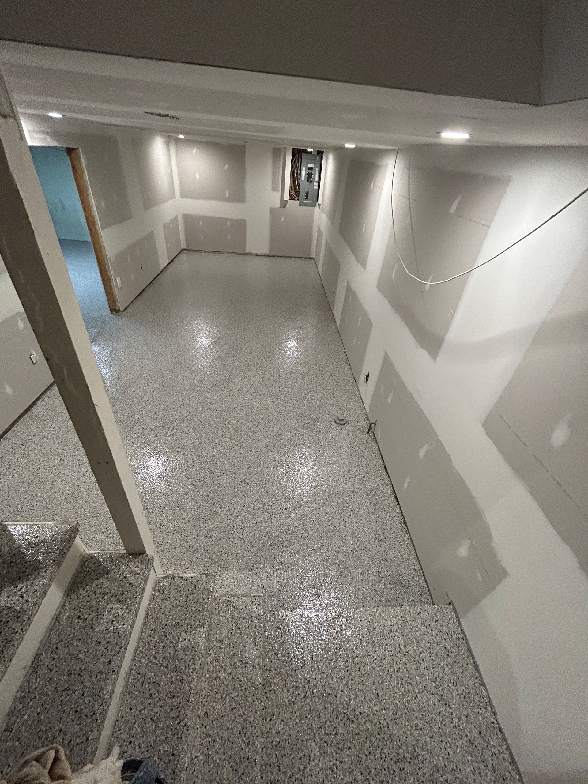 Un très long couloir avec un sol gris et des murs blancs.