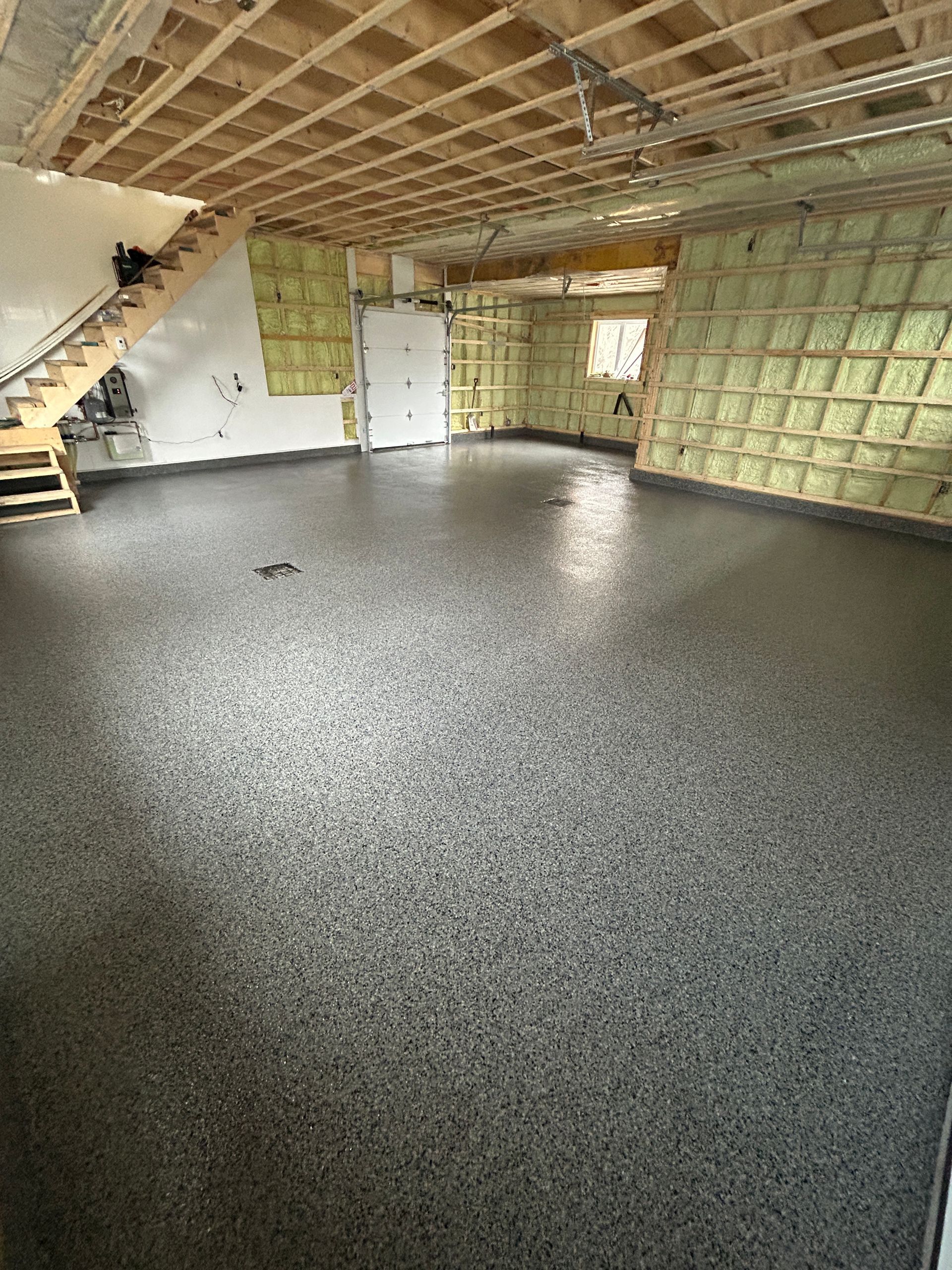 Un grand garage vide avec un escalier et un sol gris.