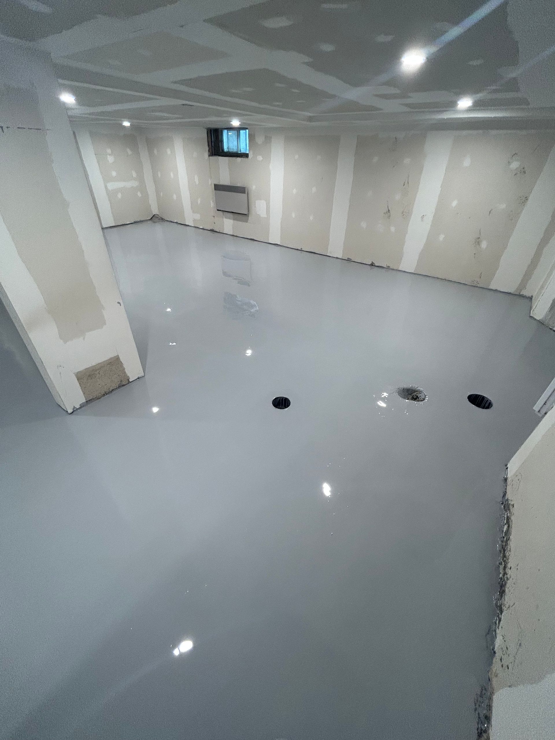 Une grande pièce avec un sol gris et des murs blancs.