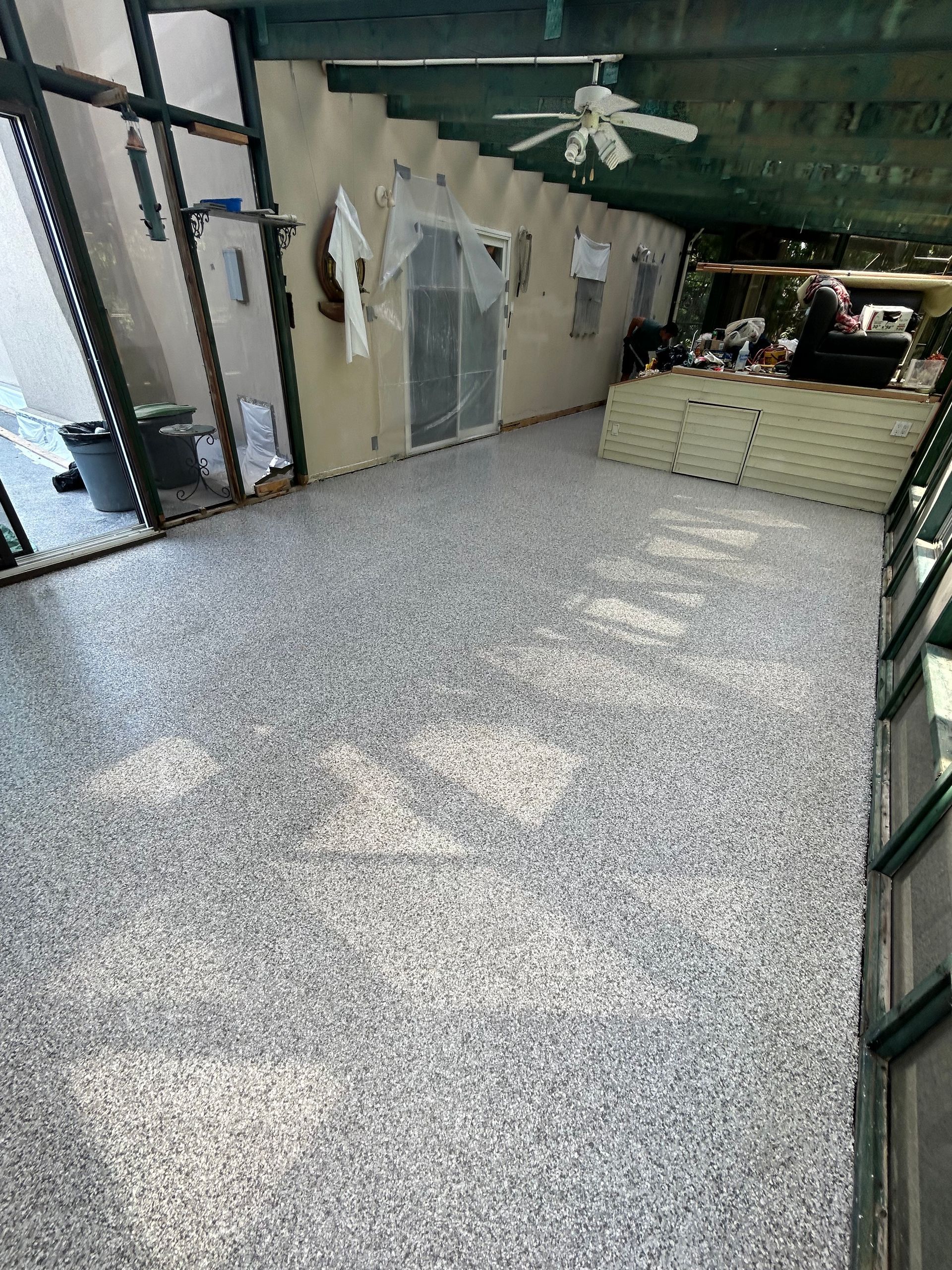 Une grande pièce avec un ventilateur de plafond et un sol gris.