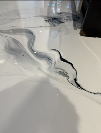 Surface abstraite grise et blanche évoquant le marbre, parcourue de stries noires fluides et présentant un coin sombre en haut à droite.