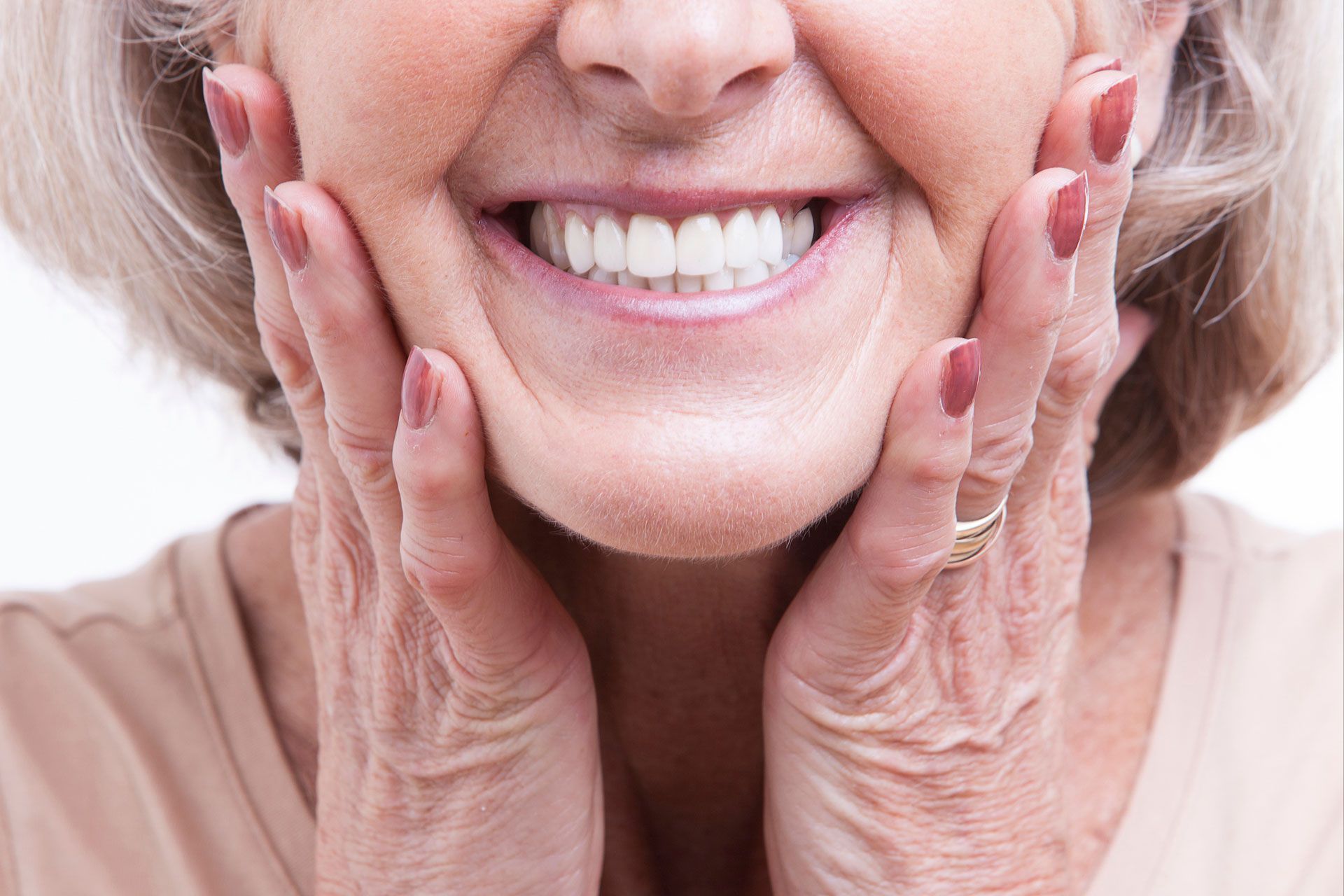 An elderly woman is smiling with her hands on her face.