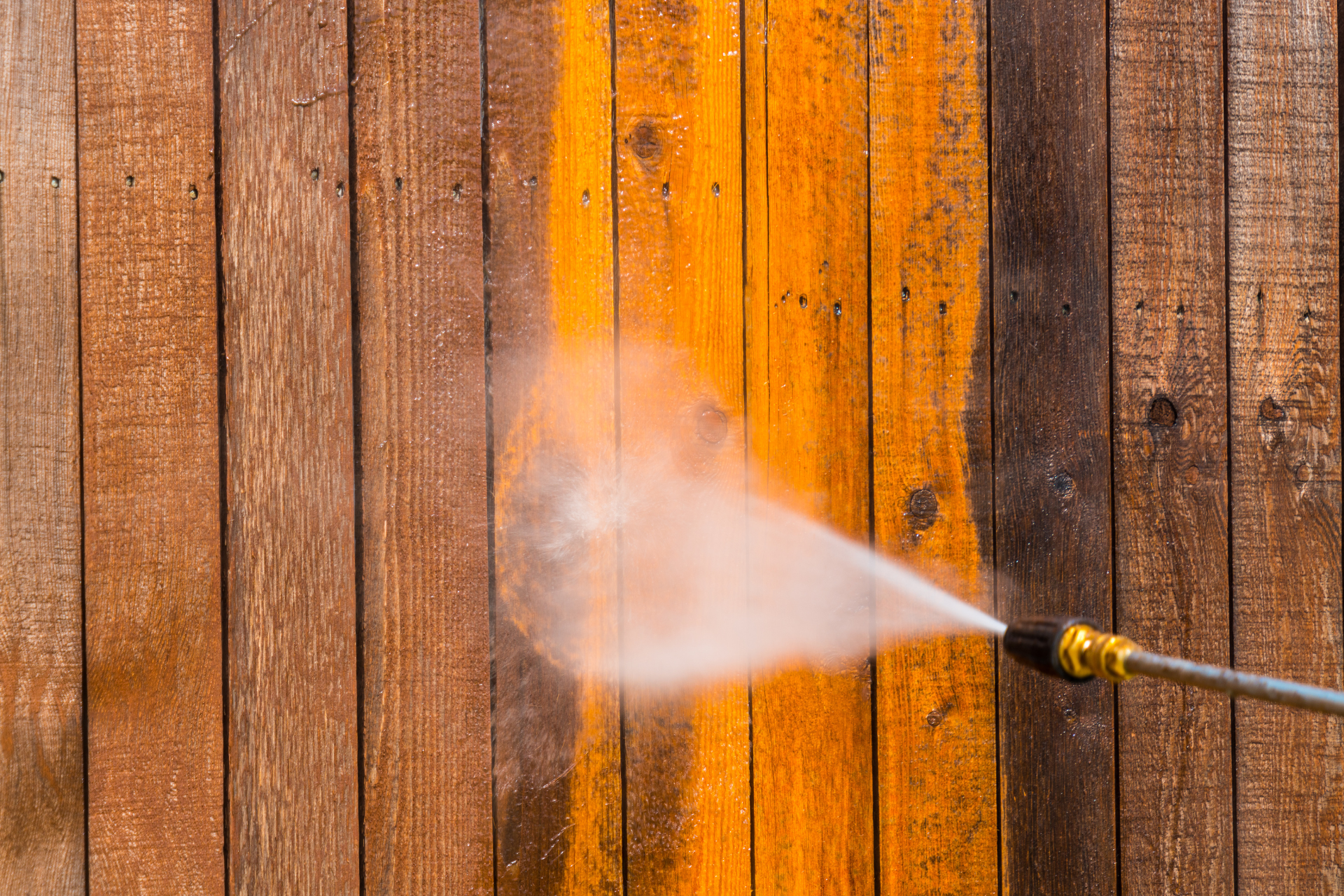 A person is using a high pressure washer to clean a wooden fence.