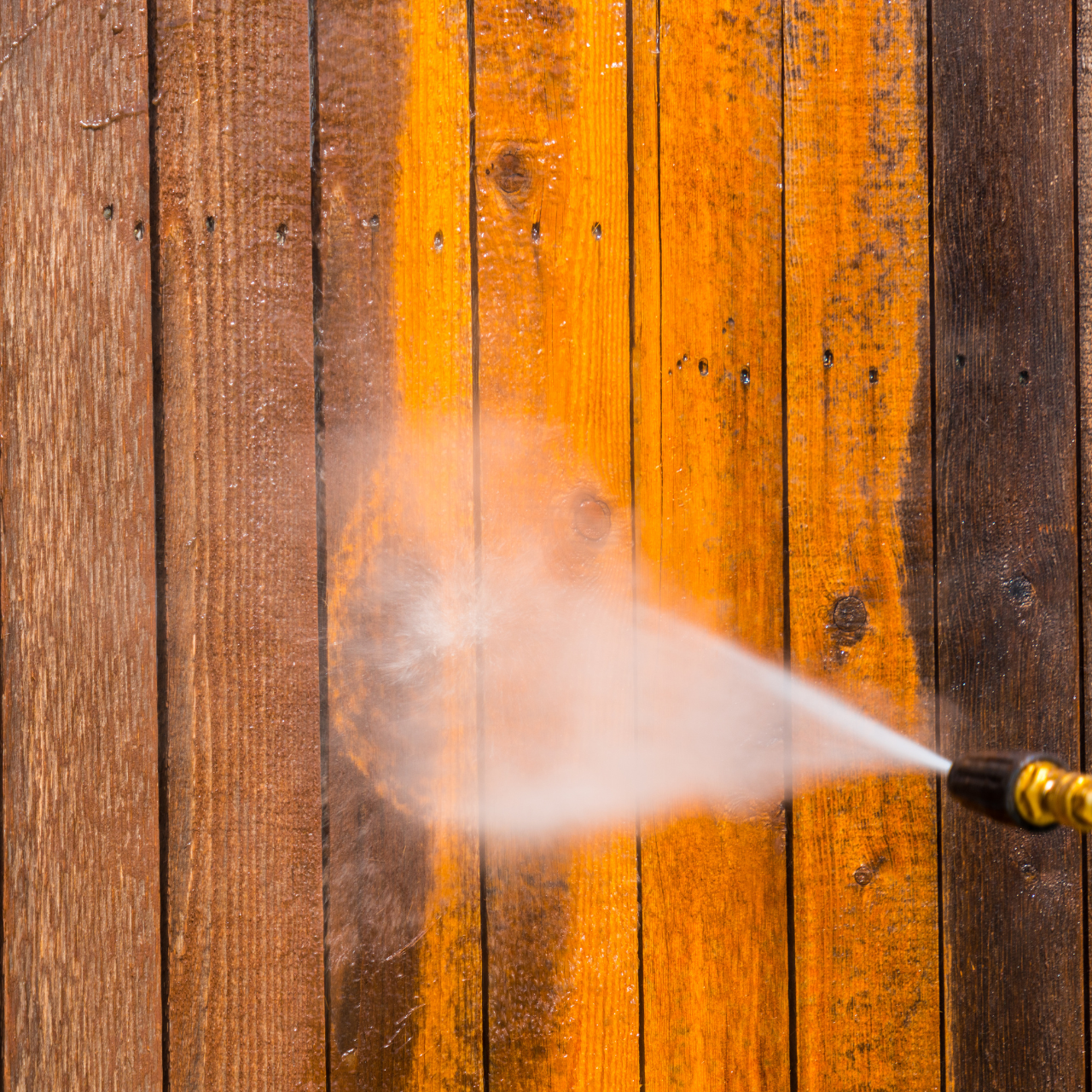 A person is using a high pressure washer to clean a wooden fence.