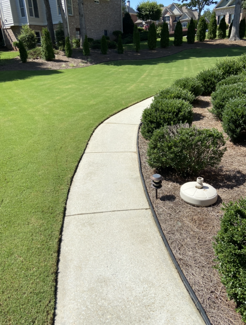 A clean concrete walkway leading to a house with a lush green lawn.