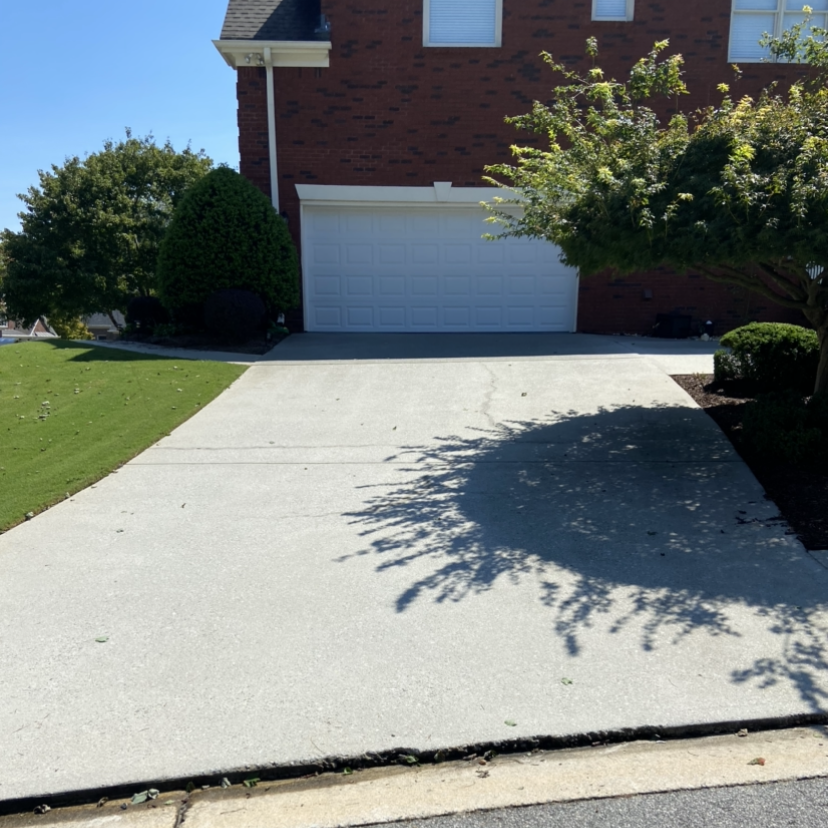 A pressure cleaned driveway leading to a brick house with a white garage door