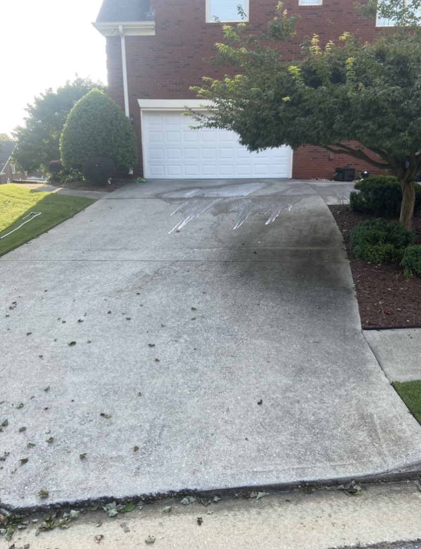 A dirty concrete driveway in front of a brick house.