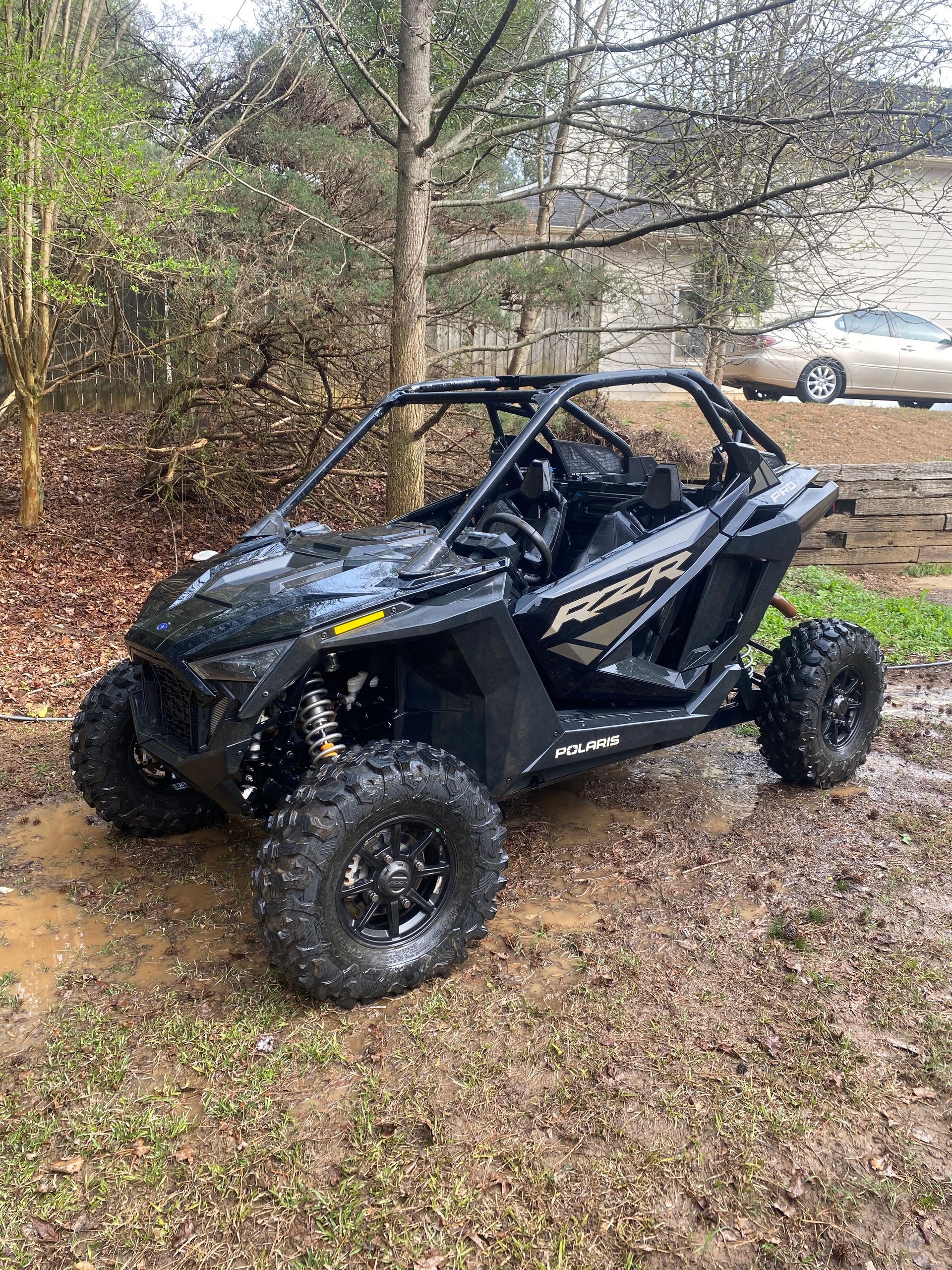 A pressure cleaned polaris rzr xp 1000 is parked in the mud in front of a house.