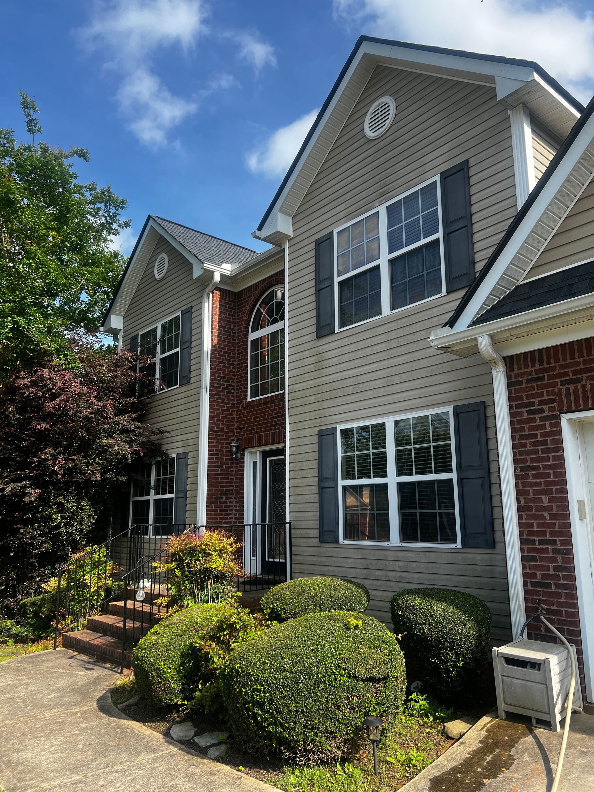 A large dirty brick house with a lot of windows and bushes in front of it.
