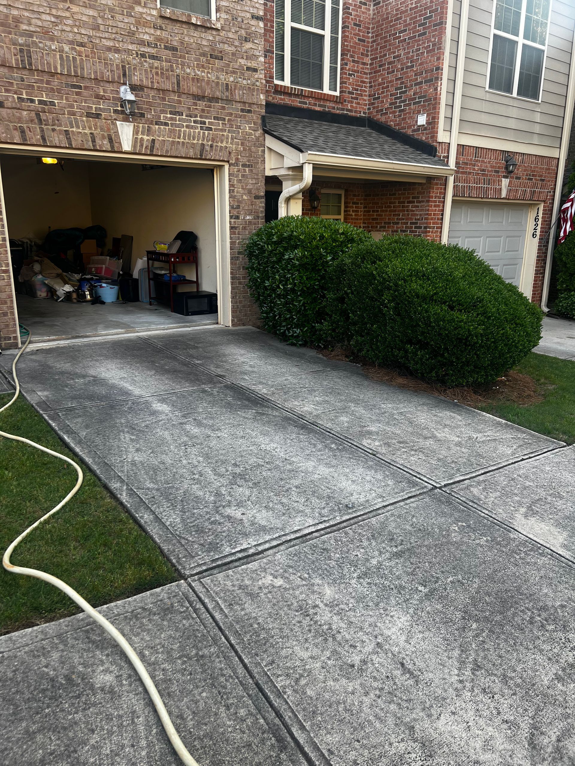 A concrete driveway in front of a brick house with a hose attached to it.