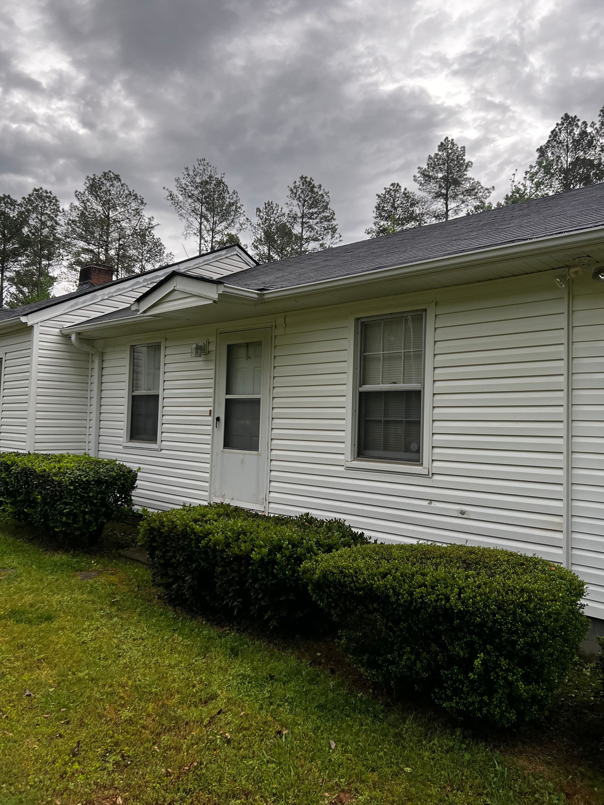 A white house with a gray roof and a lot of bushes in front of it.