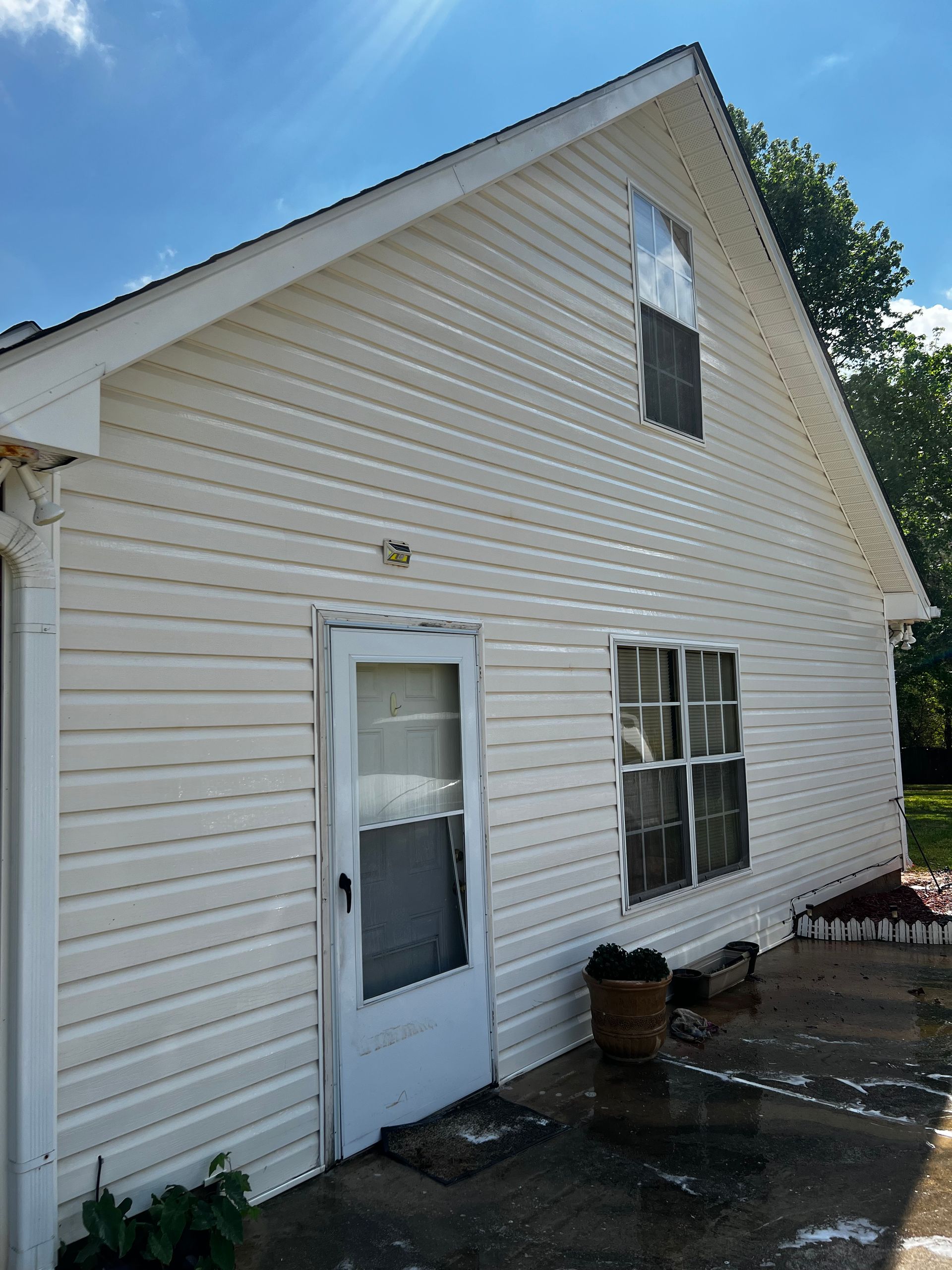 A white pressure cleaned house with a door and windows on a sunny day