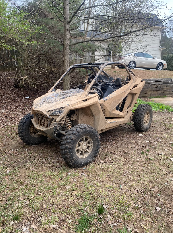 A dirty atv is parked in the dirt in front of a house.
