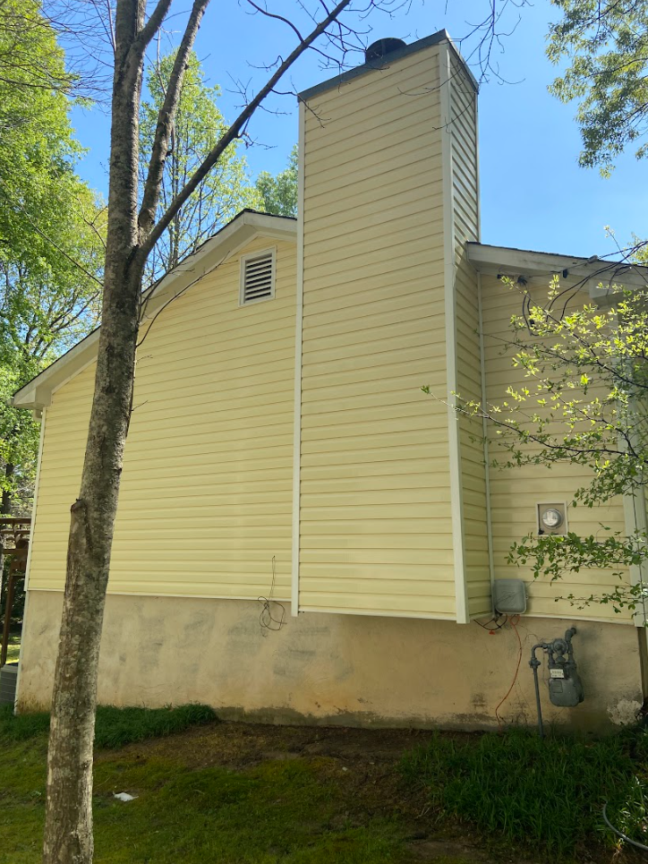 A cleaned yellow house with a chimney on the side of it.