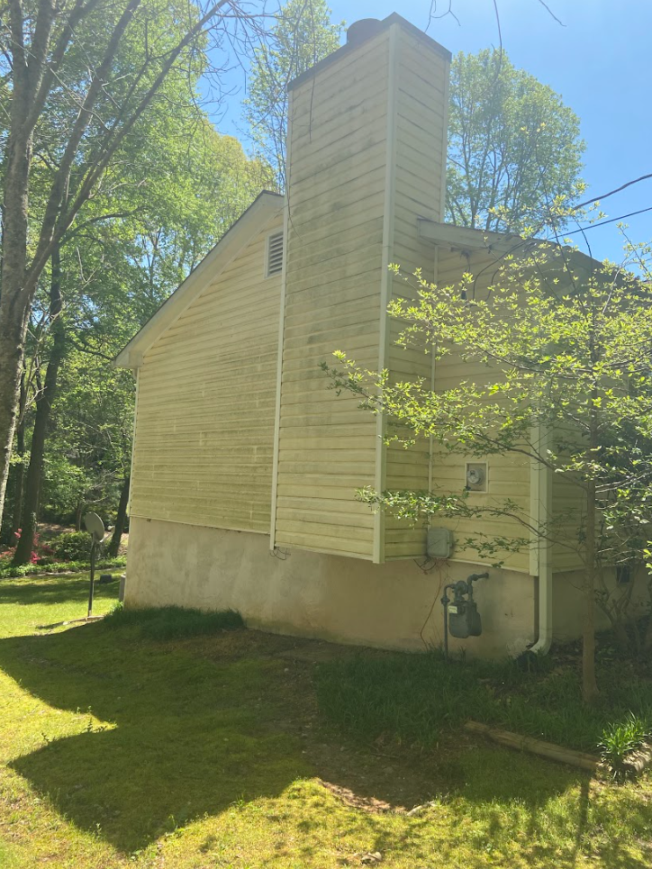 A dirty house with a chimney on the side of it is surrounded by trees and grass.