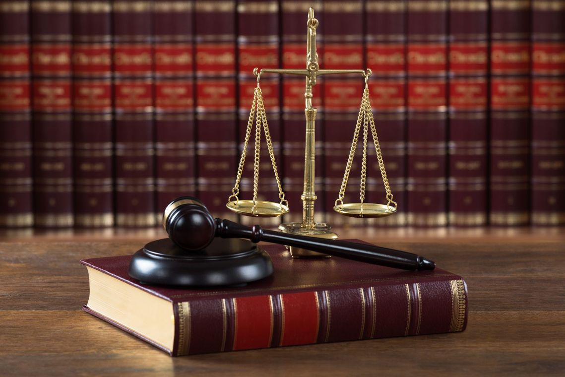 A gavel resting on a legal book in front of a set of justice scales