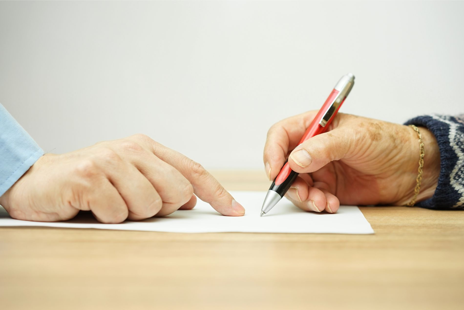 a close up of a person signing a document while being guided by an attorney