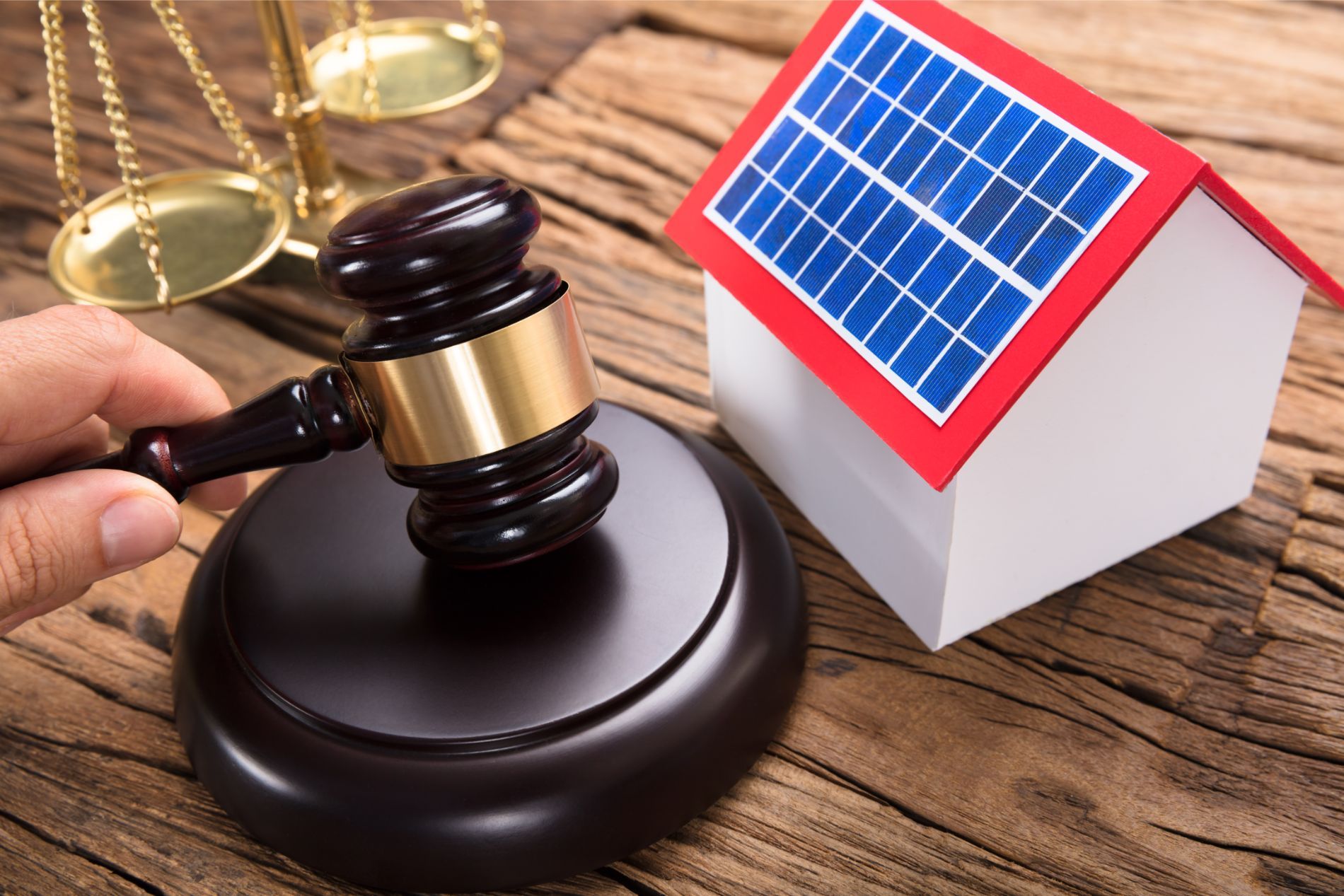 a gavel resting on a mound next to a model of a house with solar panels installed on its roof