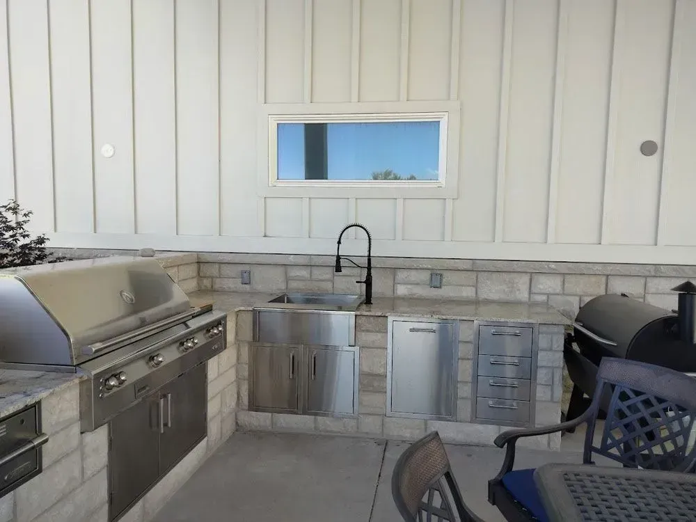 An outdoor kitchen with a grill a sink and a window