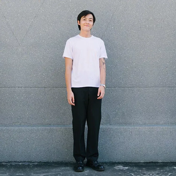 一名身穿白襯衫和黑褲子的男子站在牆前
