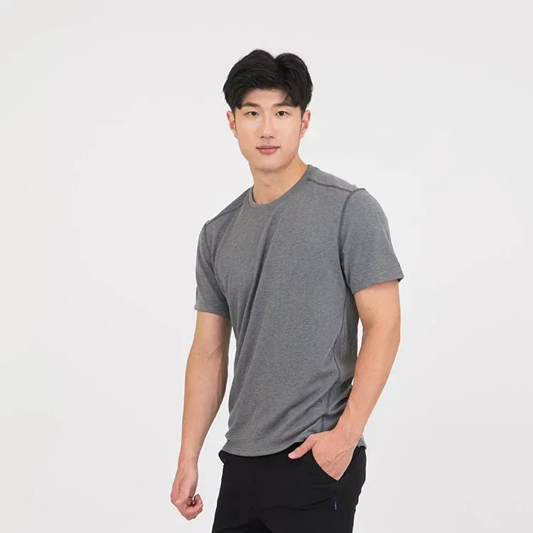 一名身穿灰色 T 恤和黑色褲子的男子站在那裡，雙手插在口袋裡。