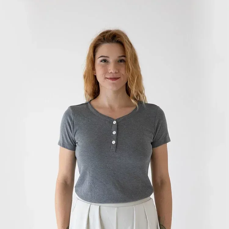 一名身穿灰色 T 恤和白色短褲的女子站在白色牆壁前。