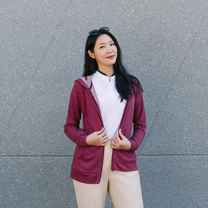 一位身穿栗色連帽衫和白色襯衫的女人站在一堵灰色的牆前。