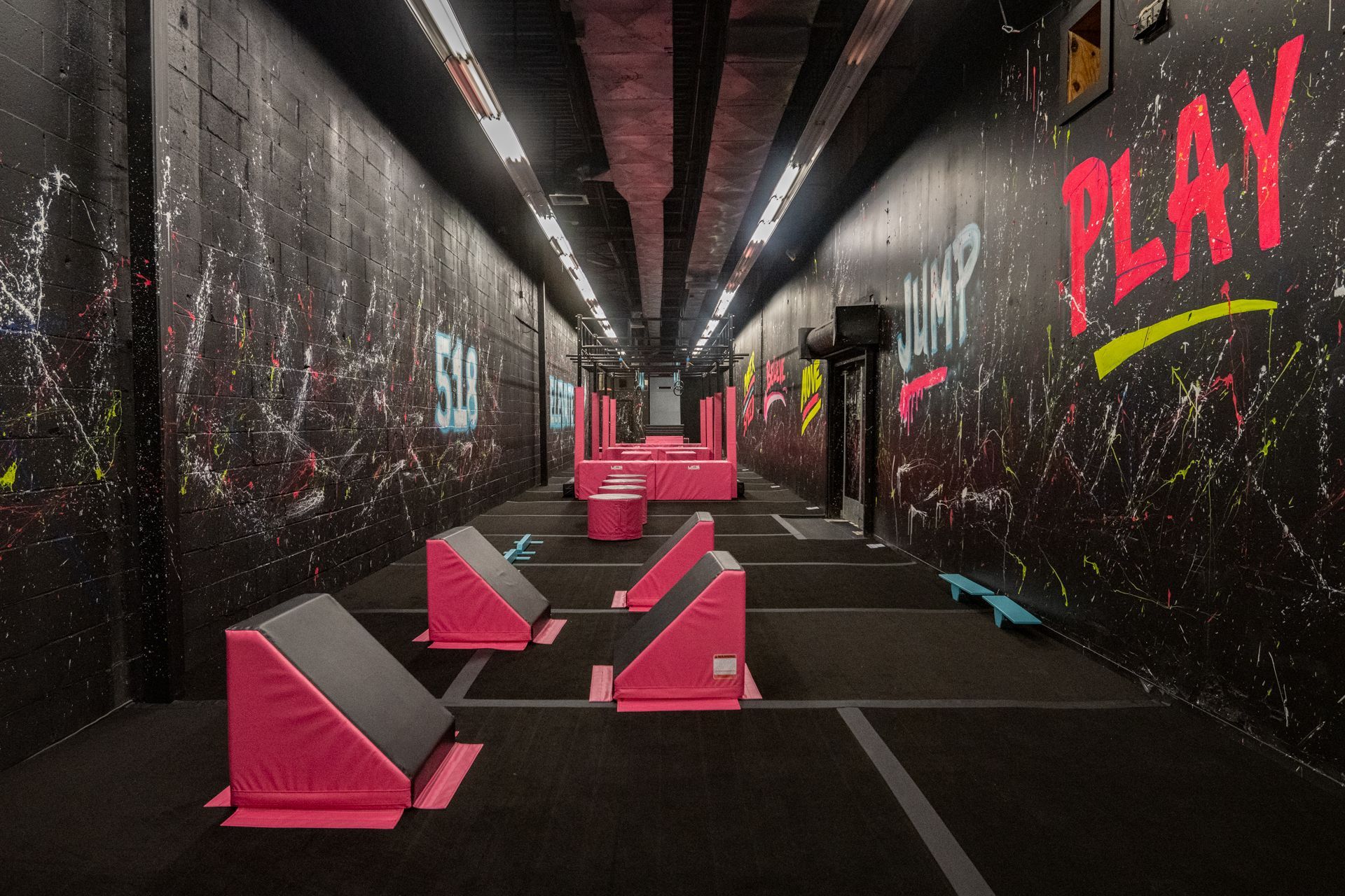 A long, narrow room with pink obstacles and graffiti-covered black walls, labeled