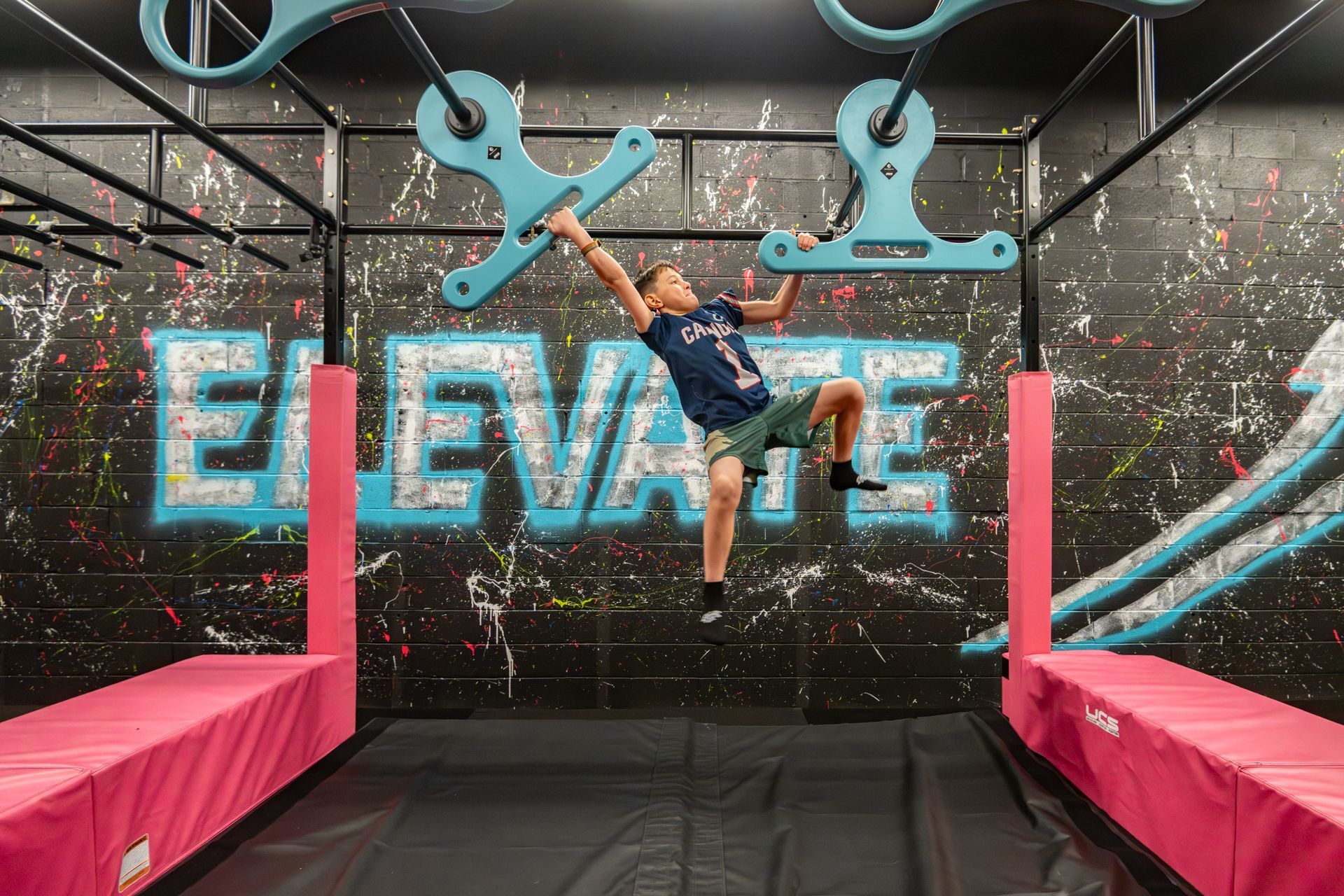 Boy hanging from blue obstacle in an indoor adventure park with