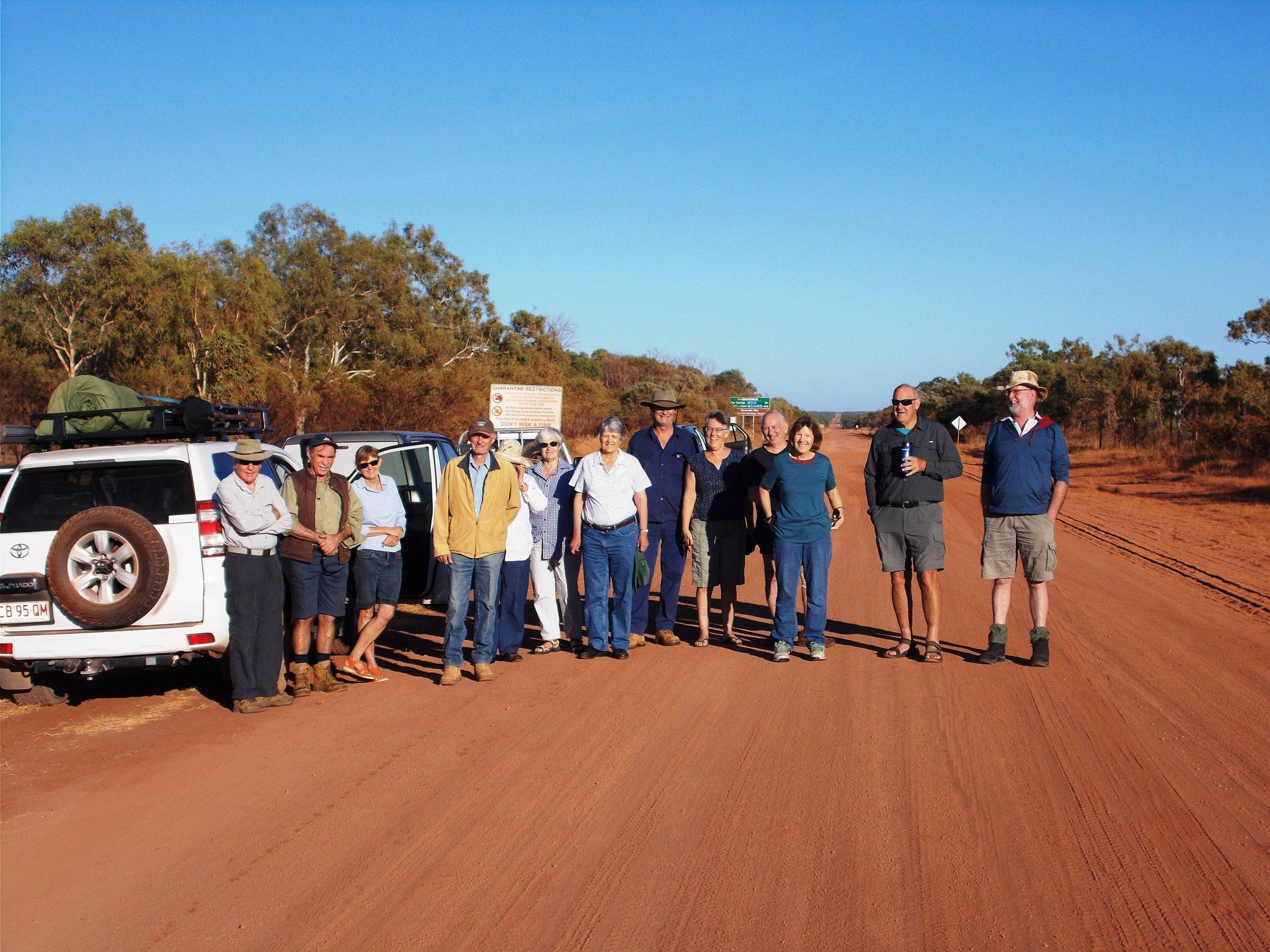 A group of people standing in front of a white suv on a dirt road