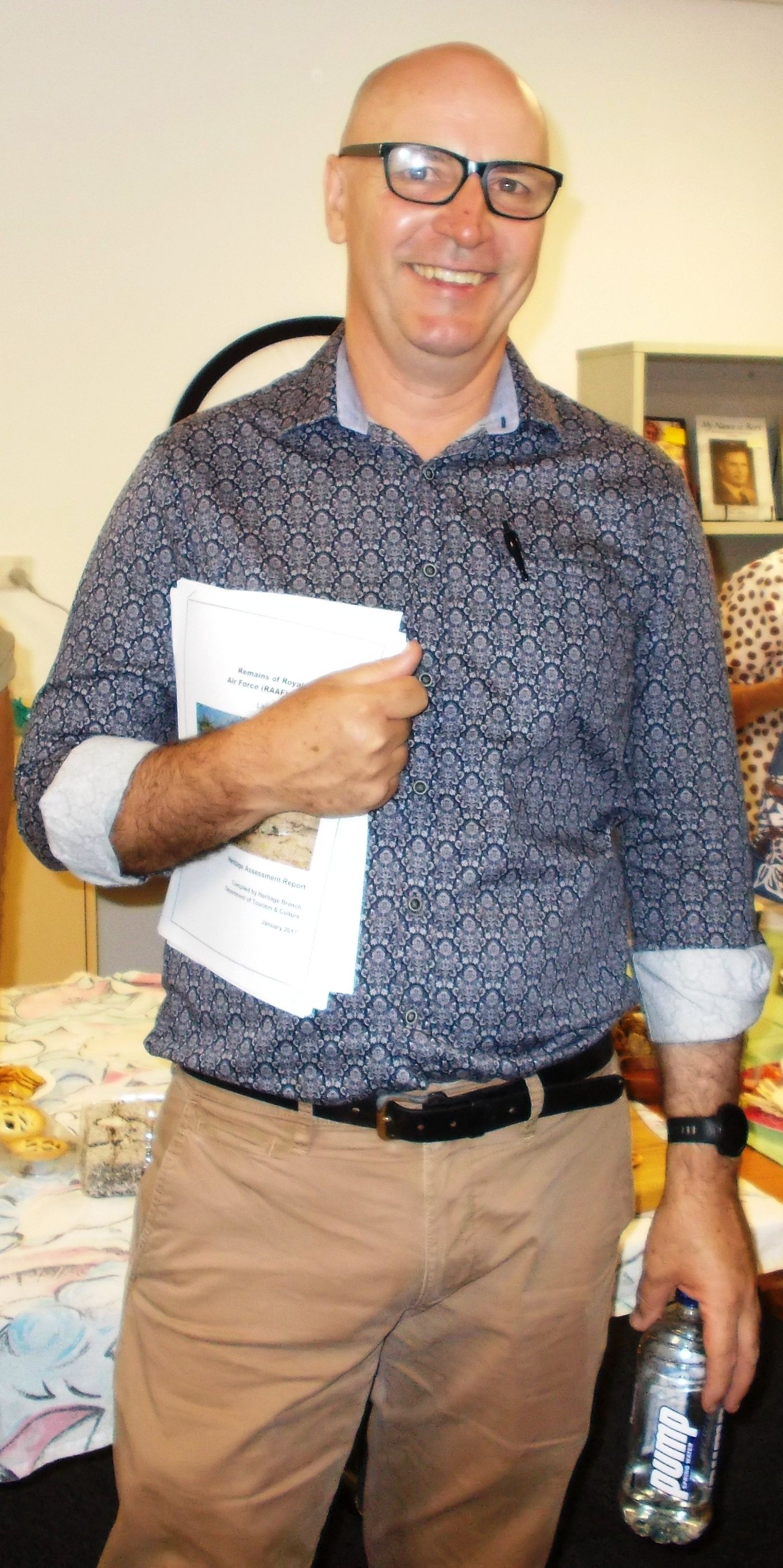 A man wearing glasses is holding a book and a bottle of water.