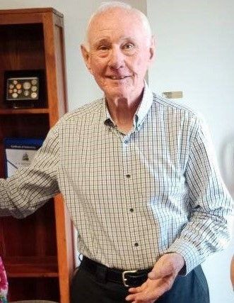 A man in a plaid shirt is standing in front of a bookshelf.