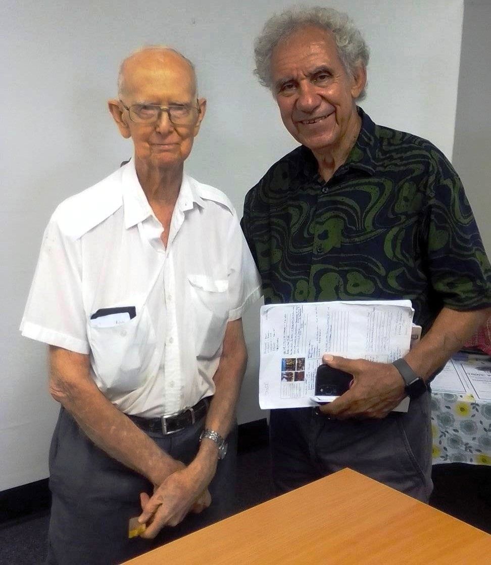 Two men are standing next to each other and one is holding a piece of paper
