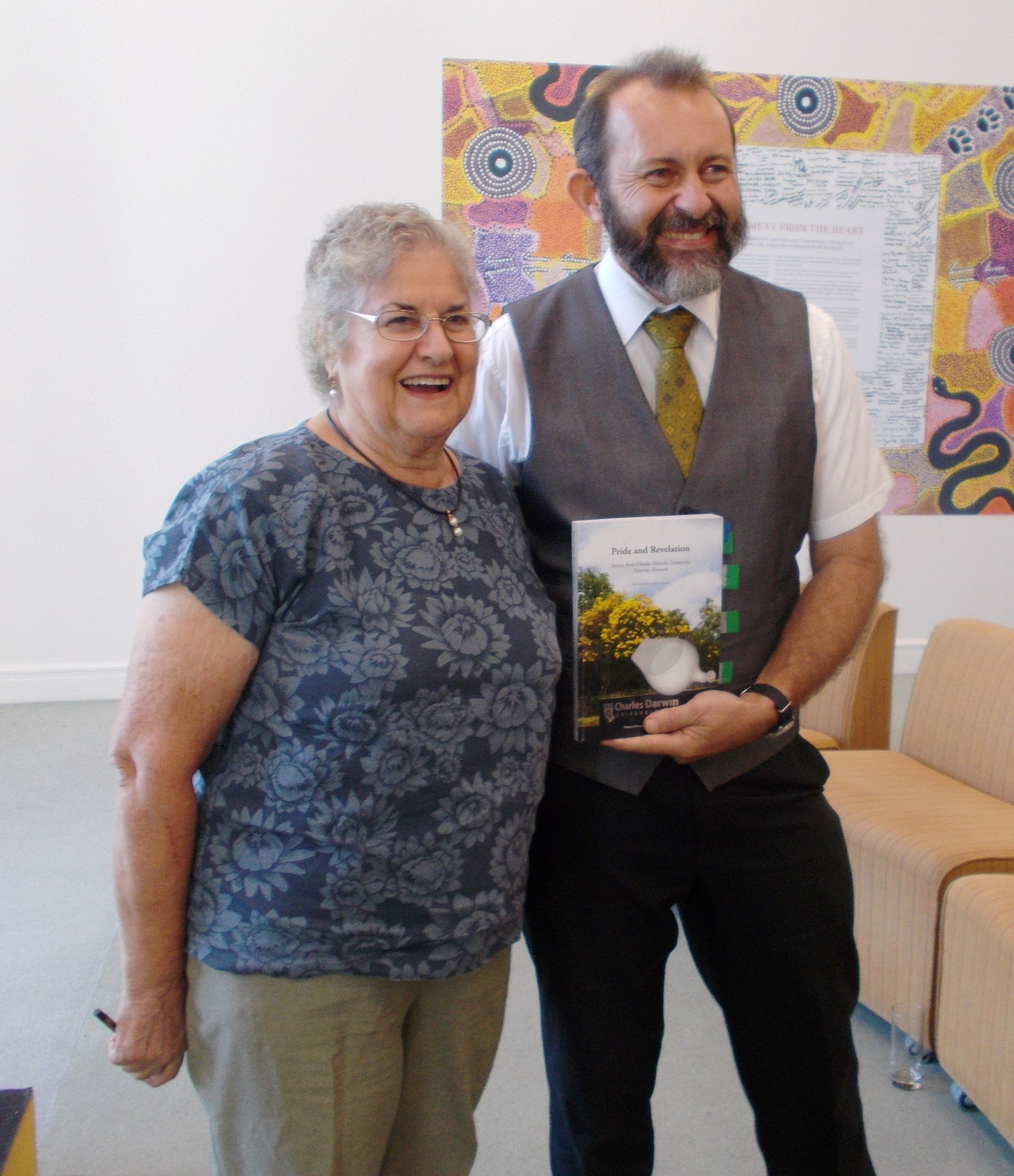 A man and a woman are posing for a picture and the man is holding a book