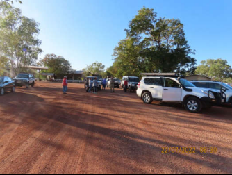 A group of cars are parked in a dirt lot