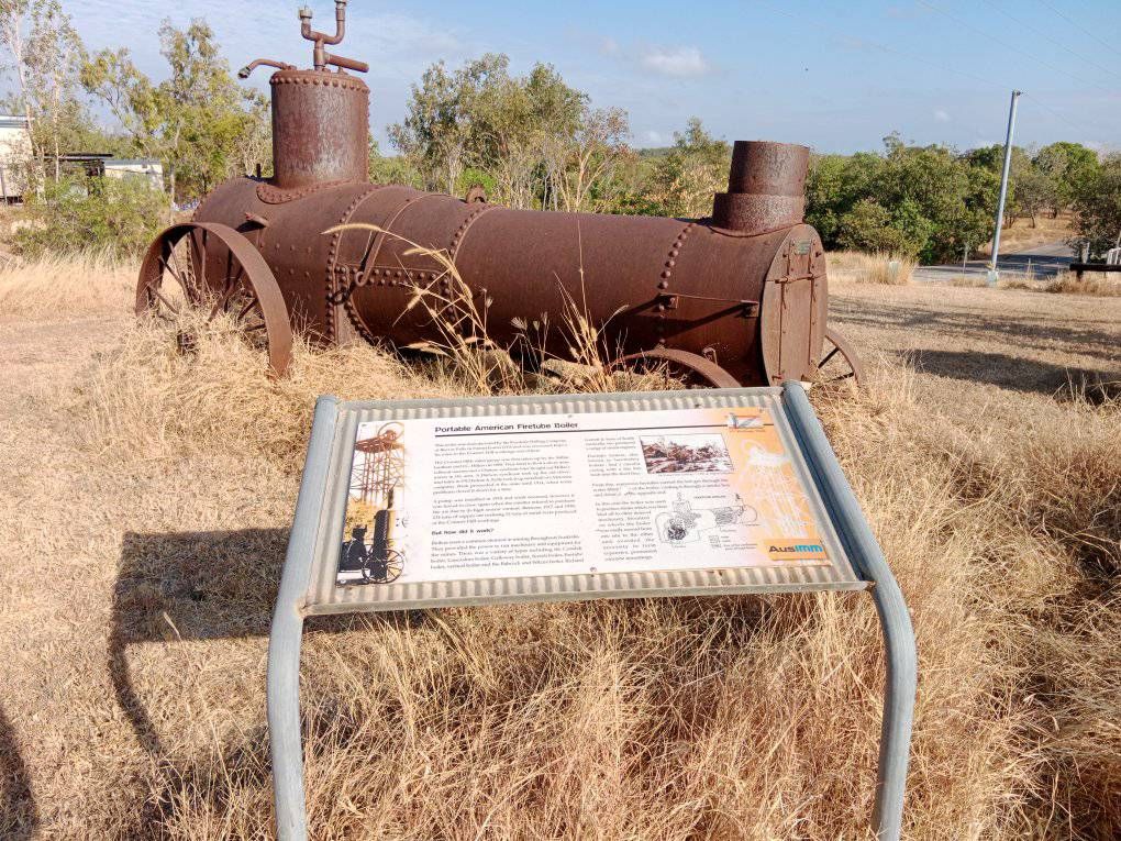 A rusty object is sitting in a field next to a sign