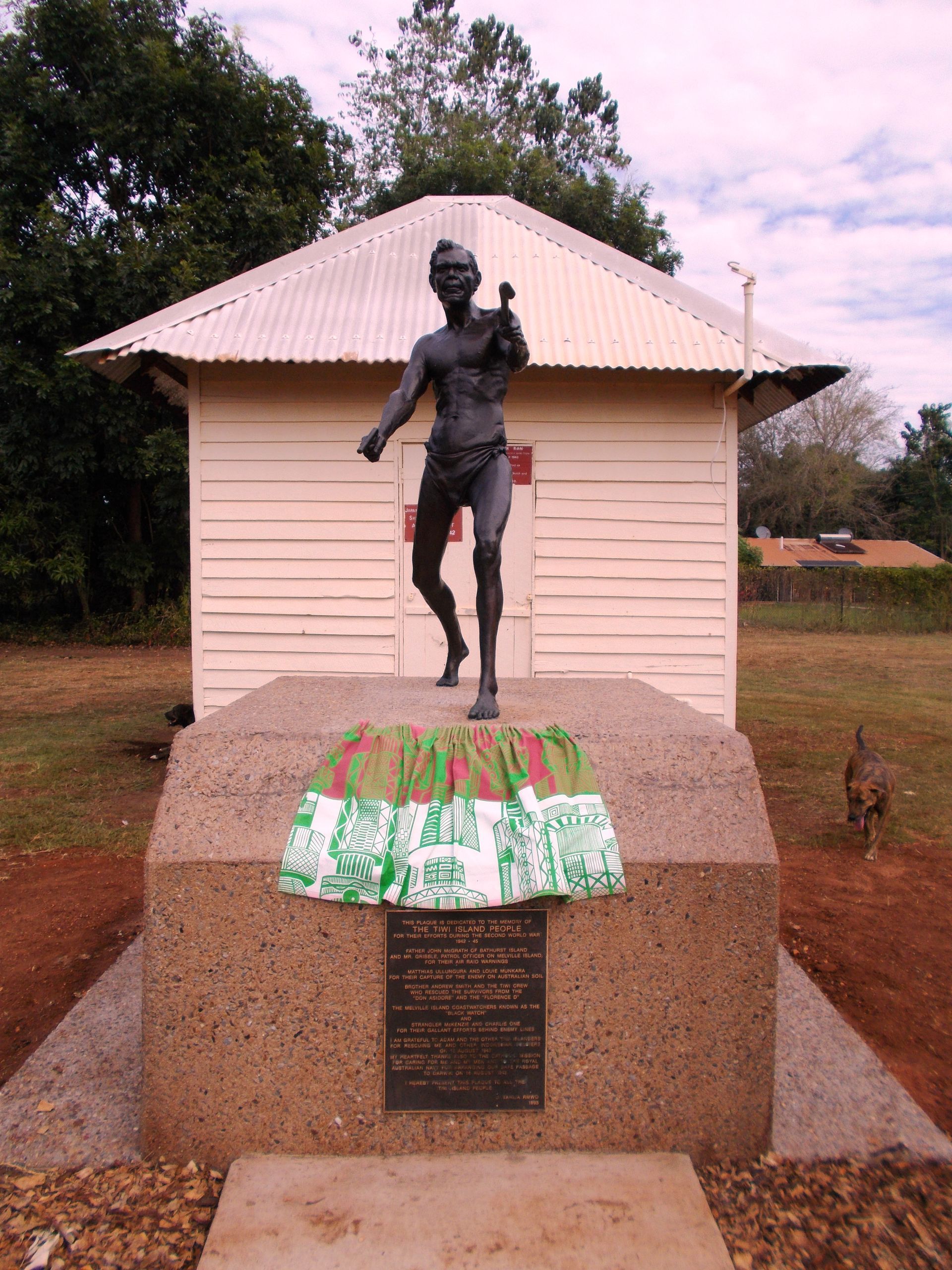 A statue of a man holding a hammer in front of a small building