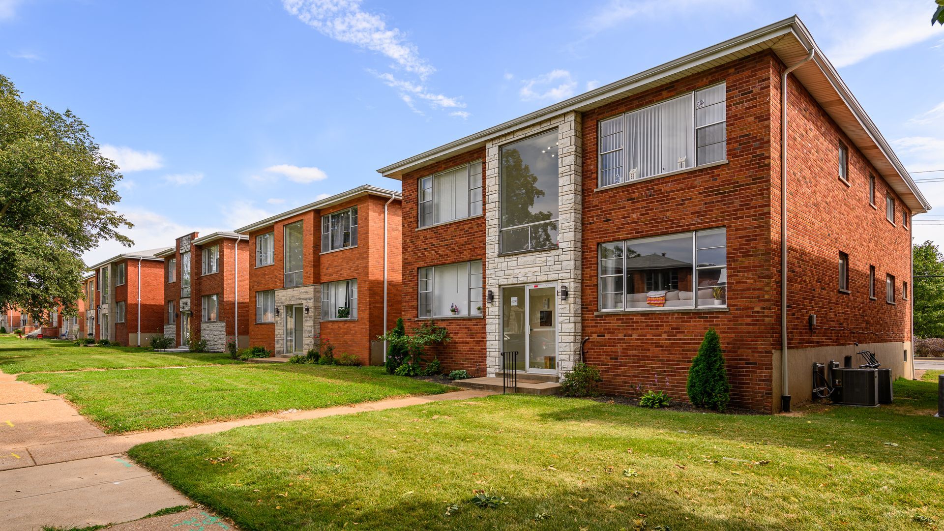 A row of brick apartment buildings with a lush green lawn in front of them.