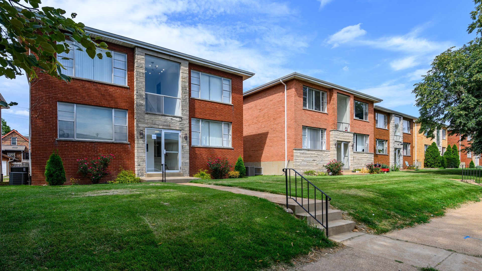 A row of brick apartment buildings with a lush green lawn in front of them.
