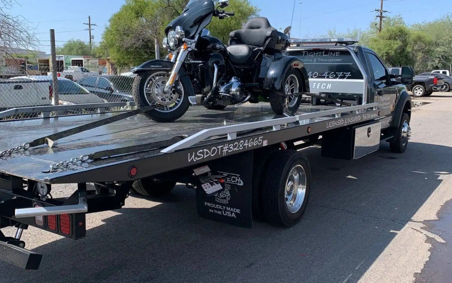 Black motorcycle on a flatbed tow truck, outdoors.