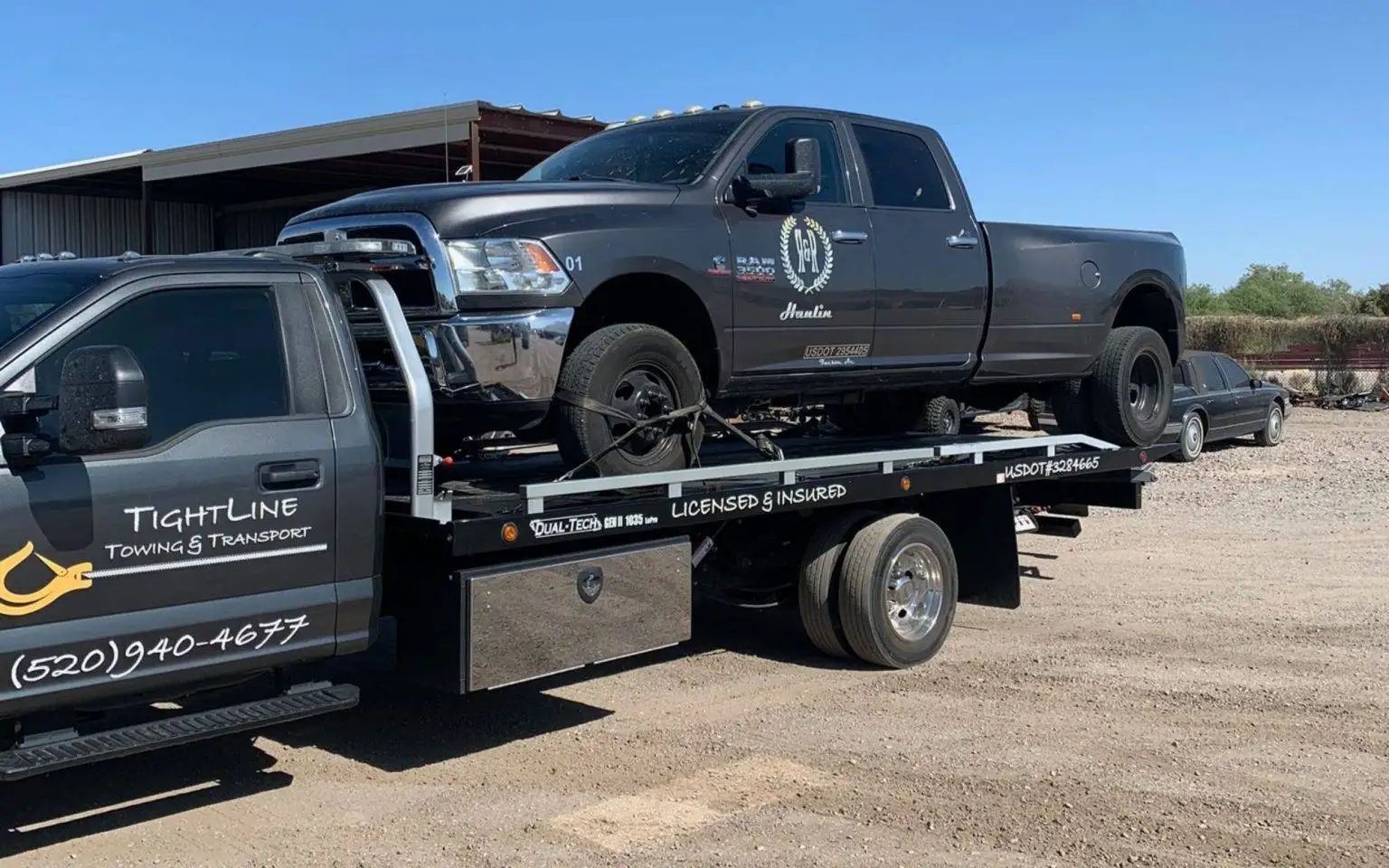 A dark gray pickup truck being towed on a flatbed tow truck under a bright sky.