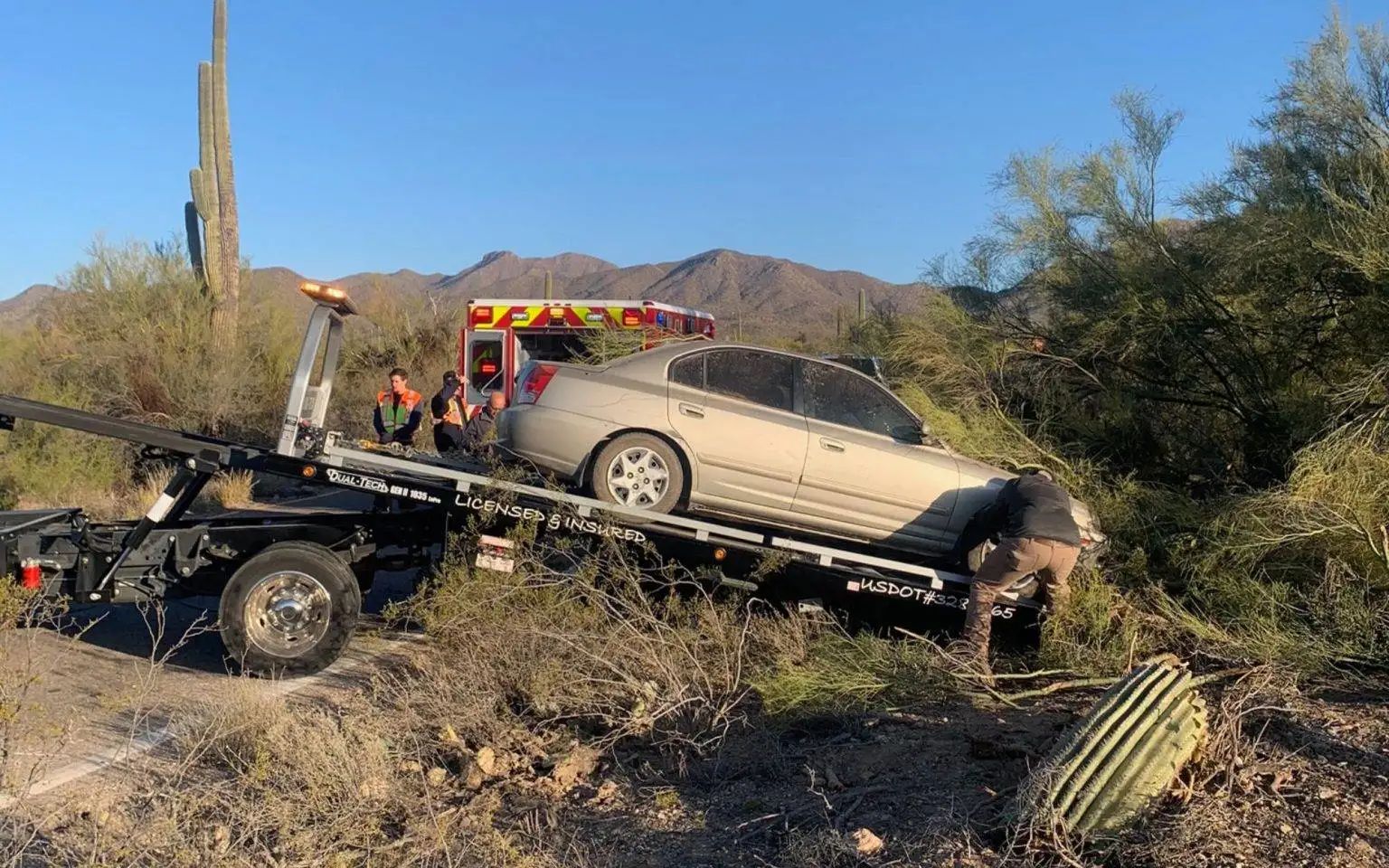 A car being towed after an accident on a desert road.